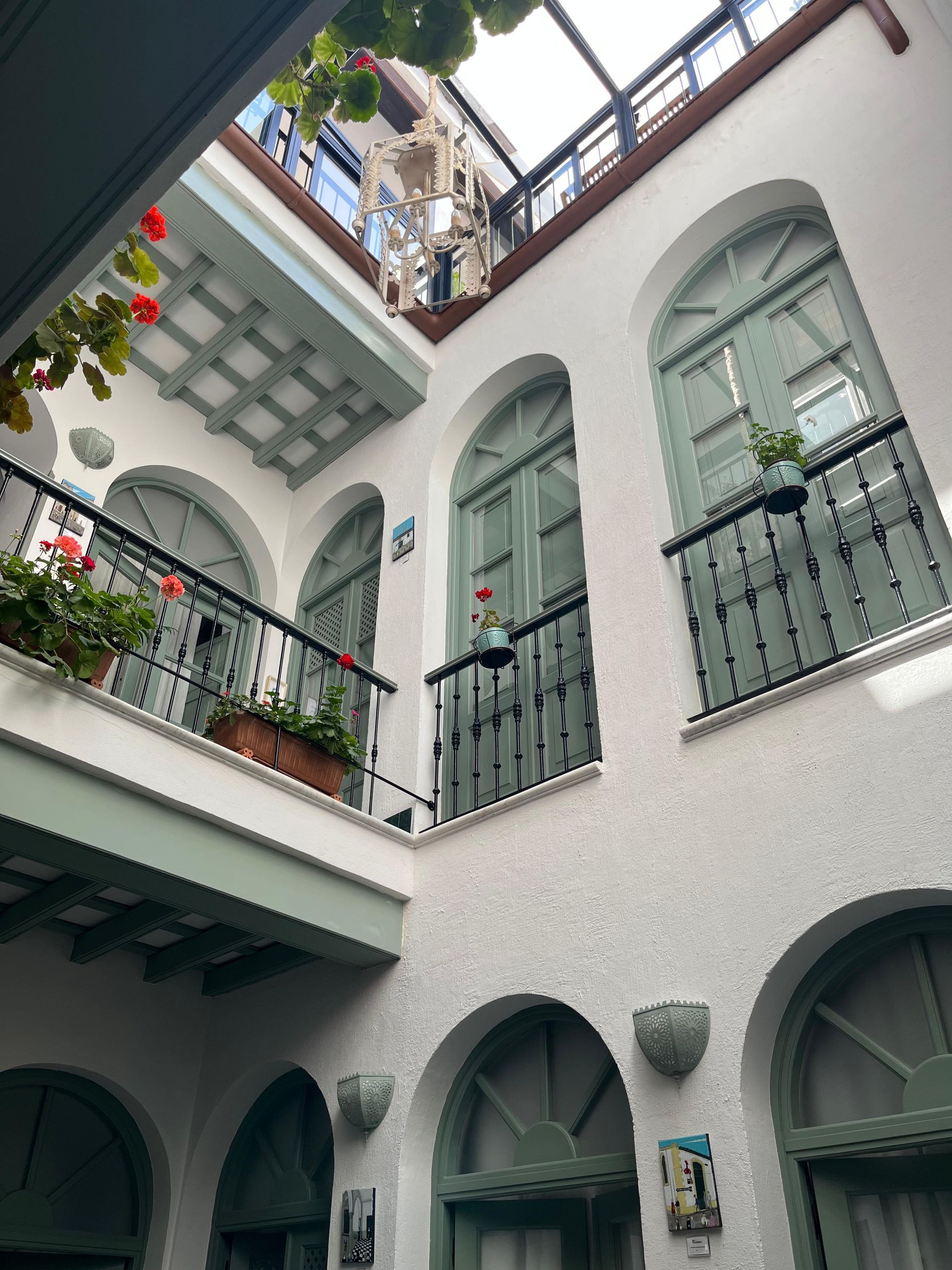 Interior de edificio de estuco blanco con puertas y balcones arqueados, molduras verdes y plantas.