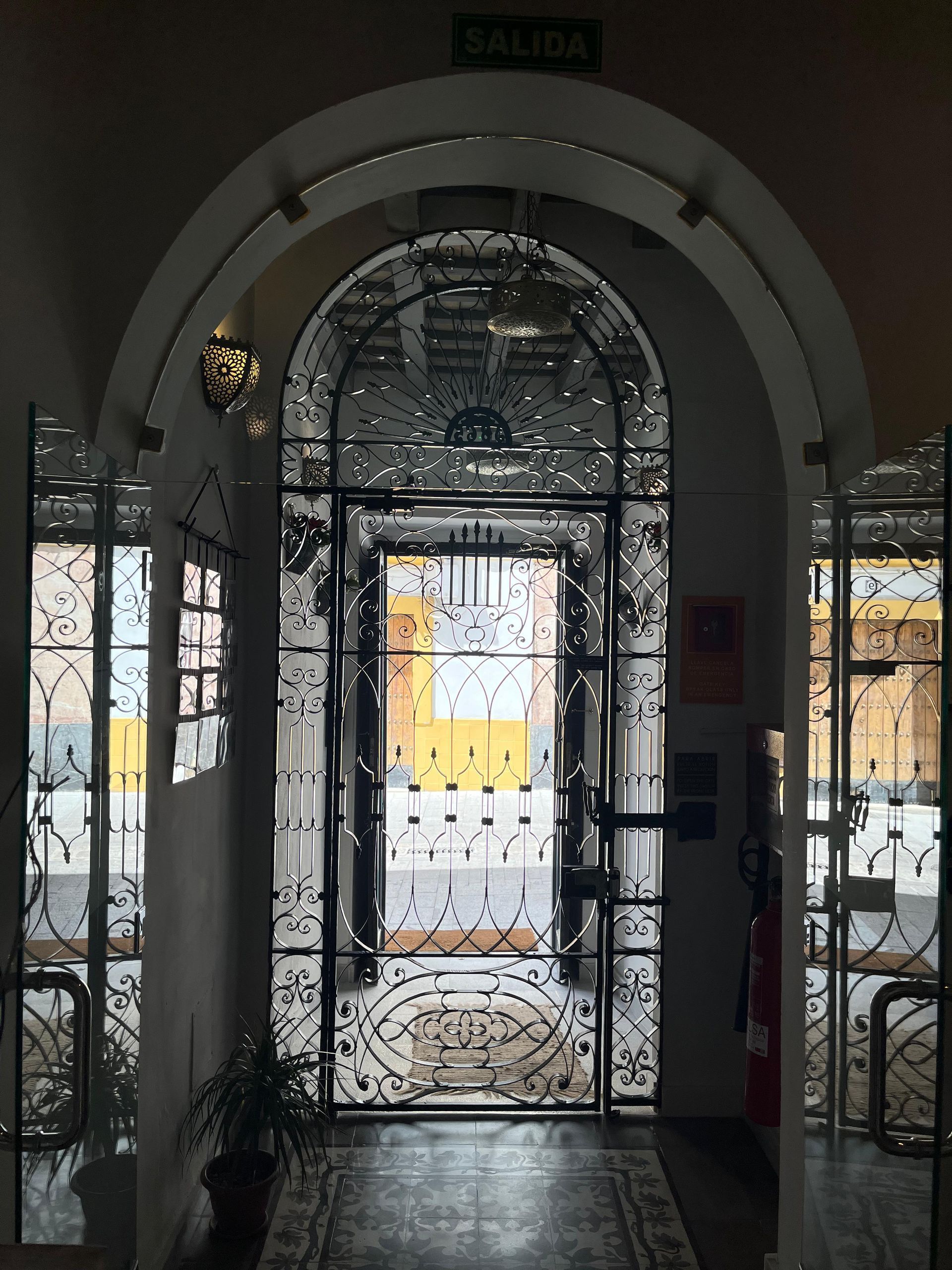 Puerta de metal negro adornada dentro de una puerta arqueada, que conduce a una calle con un edificio amarillo;