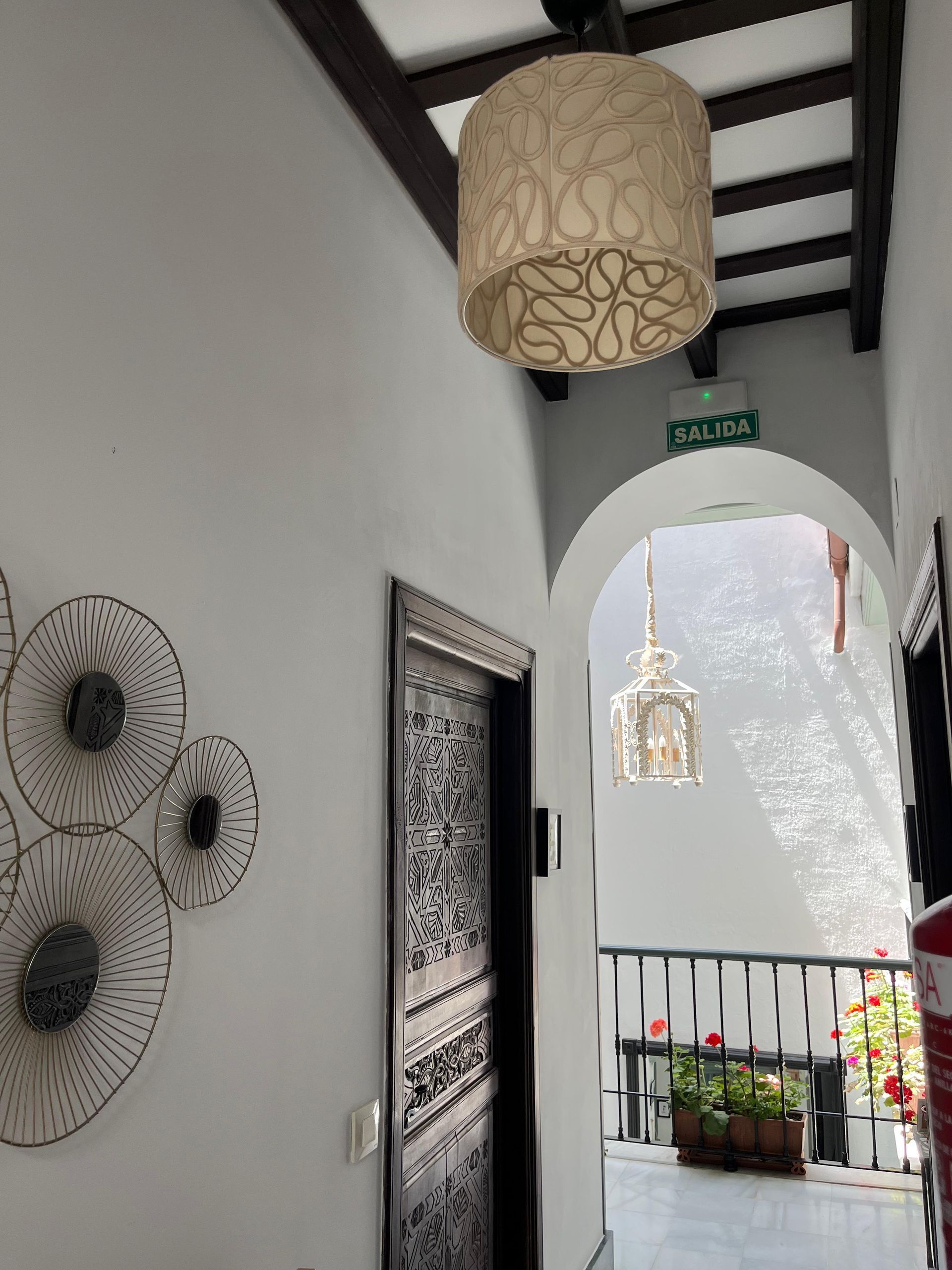 Pasillo con paredes blancas, puerta arqueada, iluminación decorativa y arte de pared de metal.