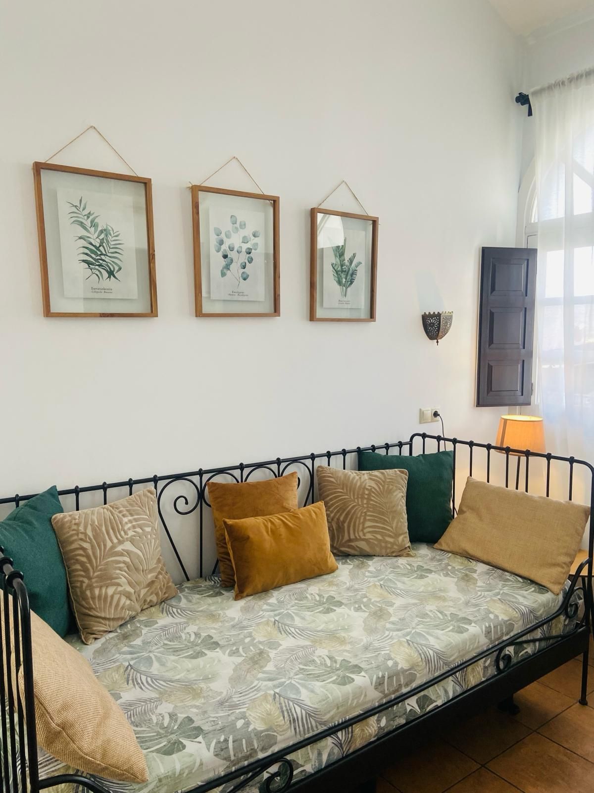 Un acogedor diván con almohadas en una habitación luminosa, con tres estampados botánicos encima.