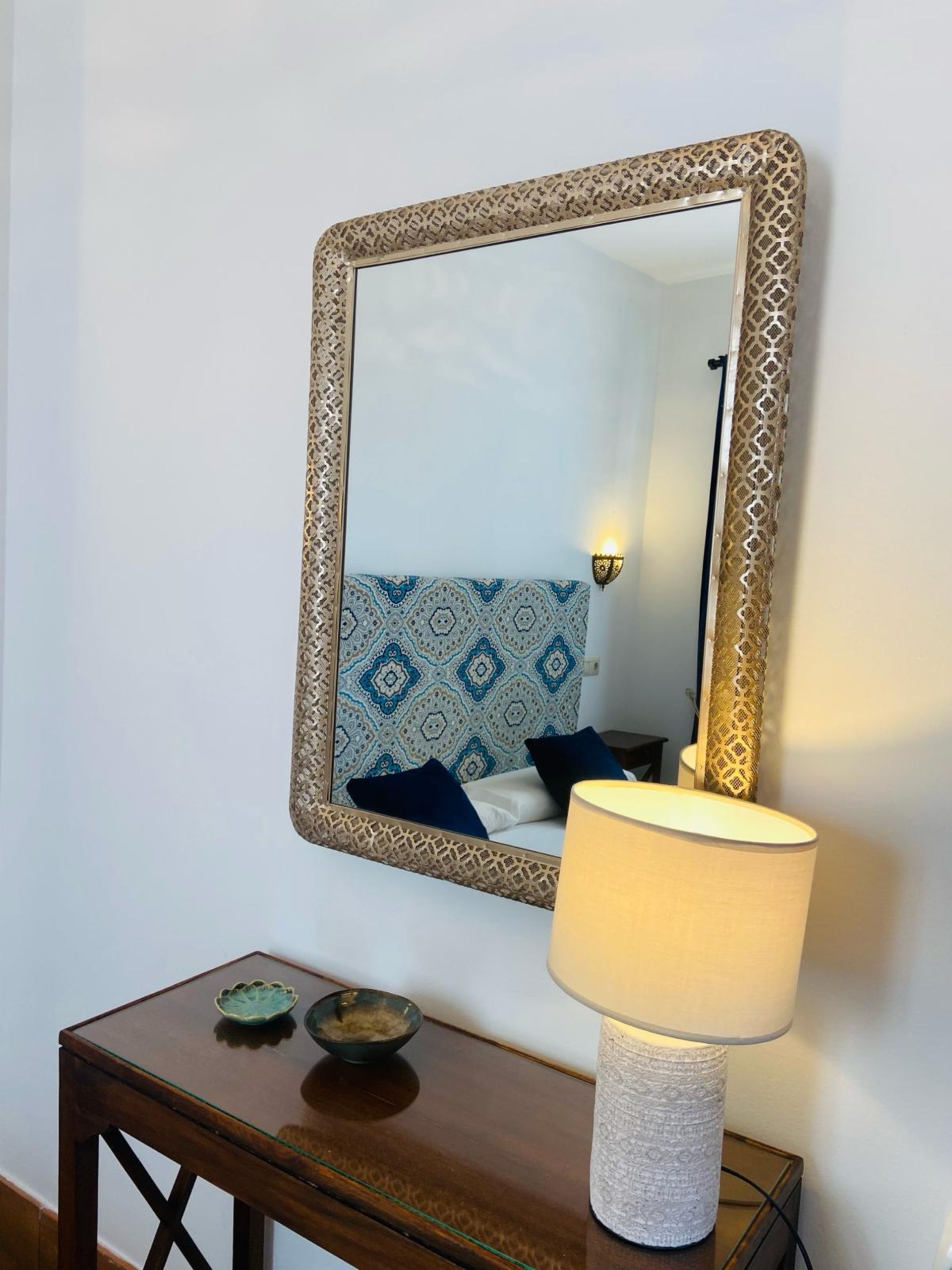 Espejo ornamentado sobre una consola de madera con lámpara y cuencos.