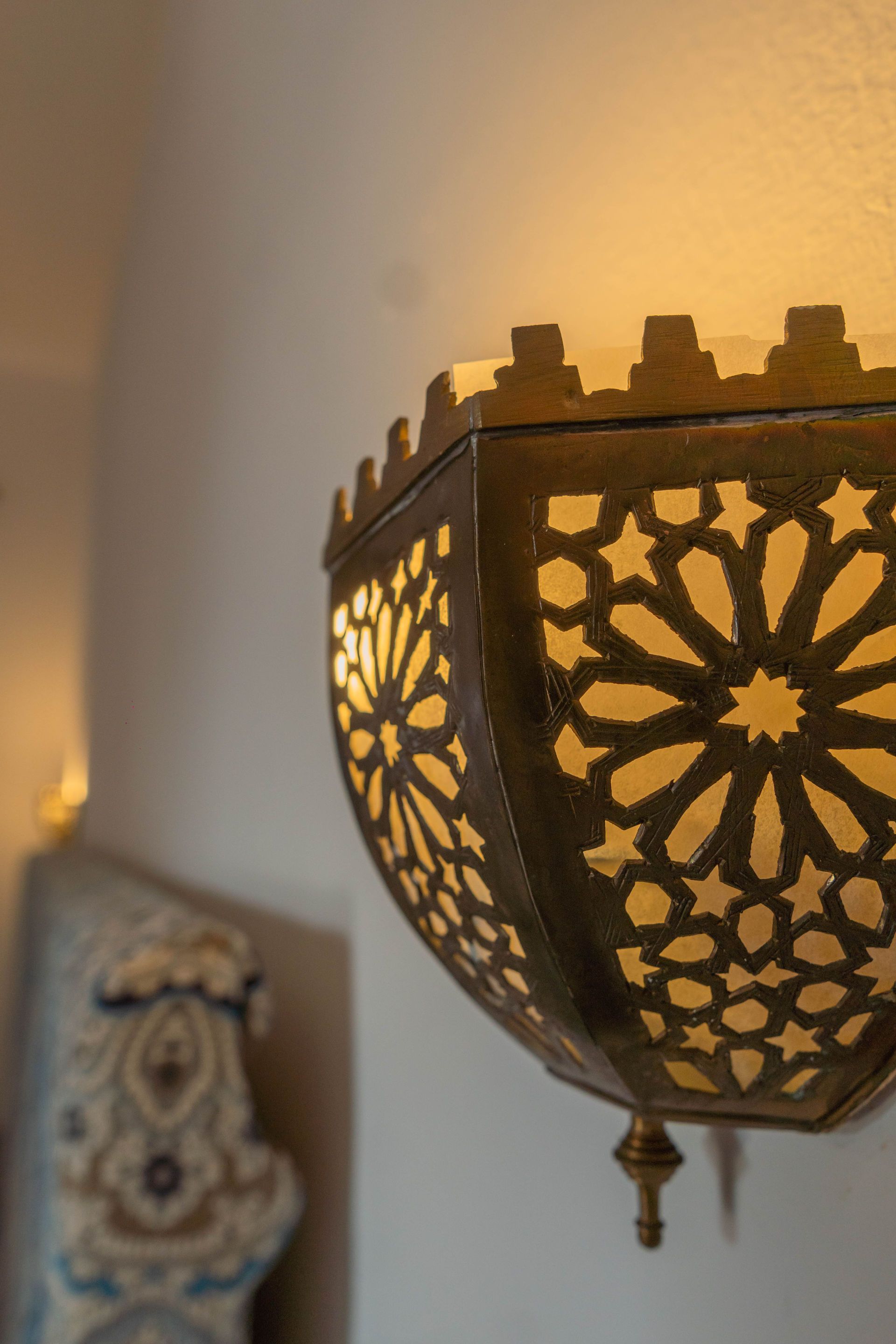 Linterna de latón adornada y brillante con intrincados patrones recortados, montada en una pared blanca.