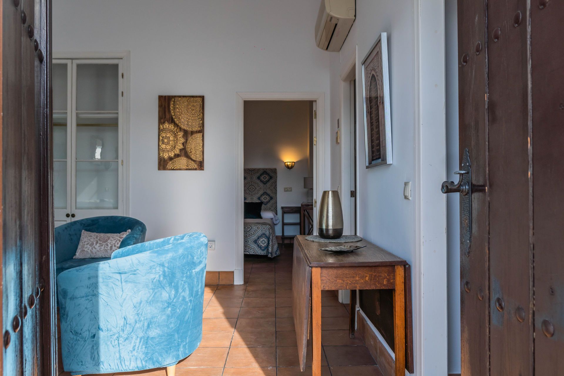 Entrada con sillón azul, consola de madera y vista a otra habitación.