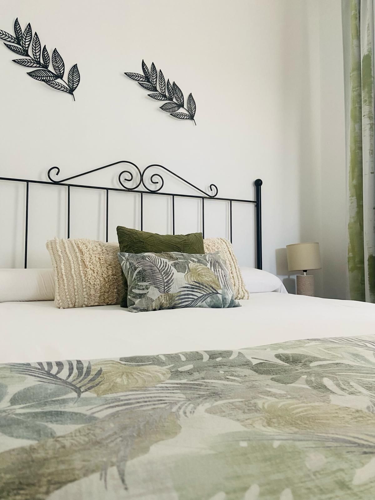 Dormitorio con cabecera de hierro forjado, ropa de cama blanca, almohadas y camino de mesa 