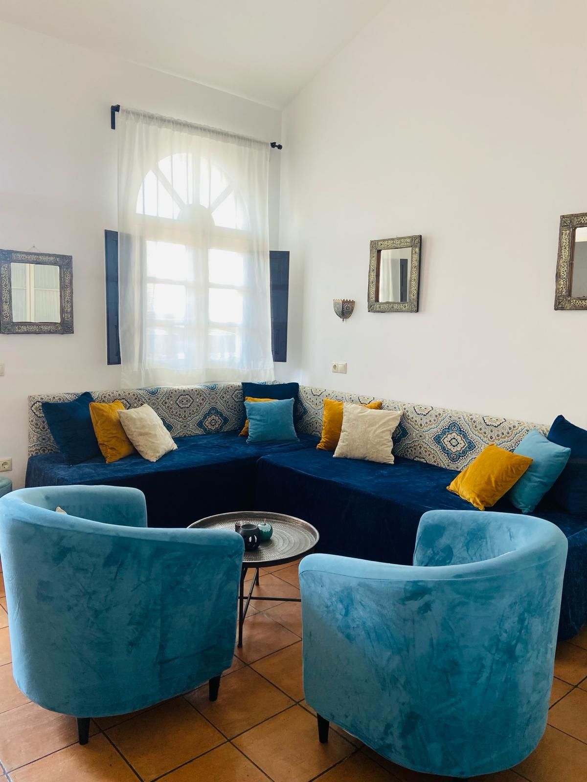 Sala de estar con sofá seccional de terciopelo azul, dos sillones verde azulado y almohadas decorativas.