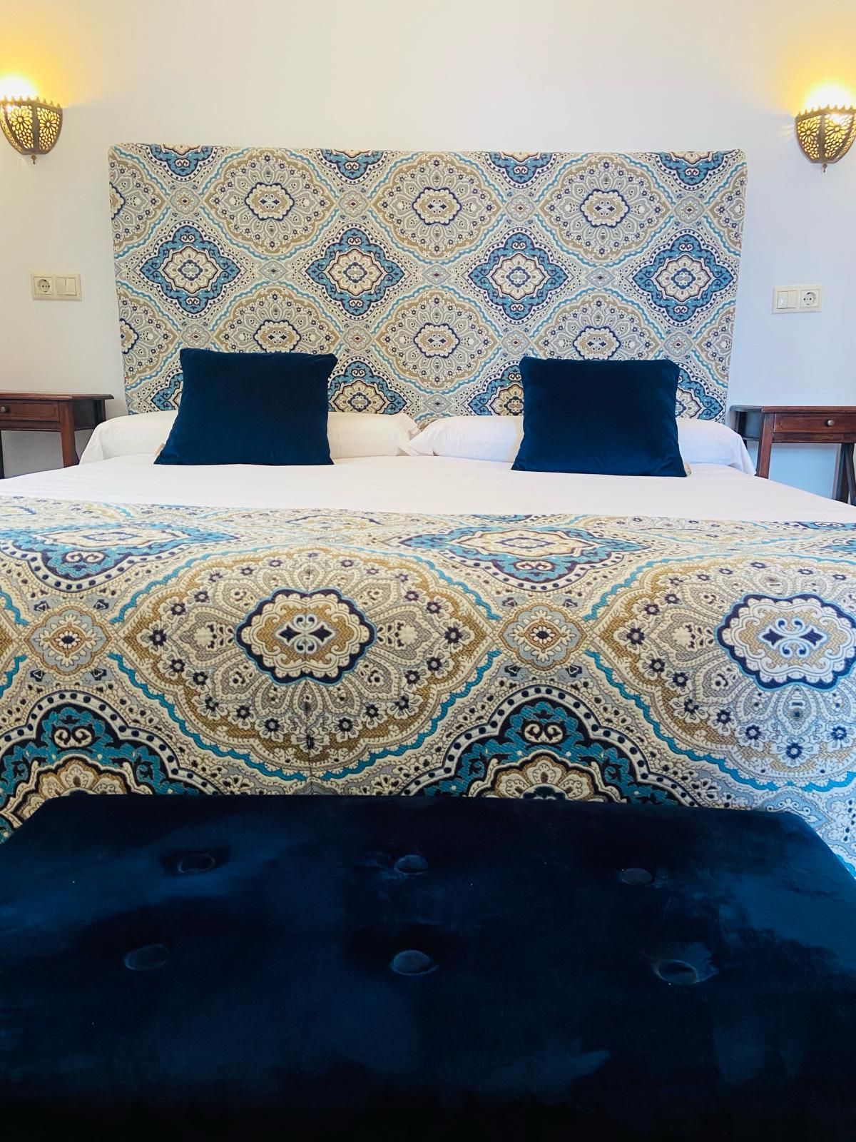 Dormitorio con cabecero, colcha y banco con estampados en azul y blanco. Dos almohadas azules sobre la cama.