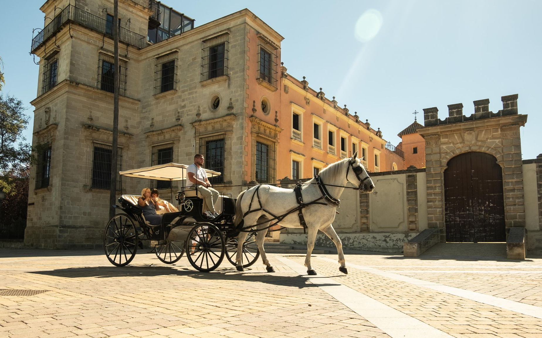 Un carruaje tirado por caballos frente a un edificio de color claro. Había gente dentro. Un día soleado y luminoso.