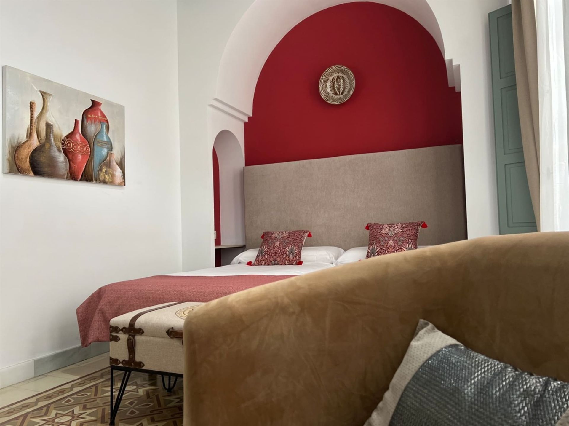 Dormitorio con pared y cama con acento rojo, sofá de tonos neutros y obras de arte.