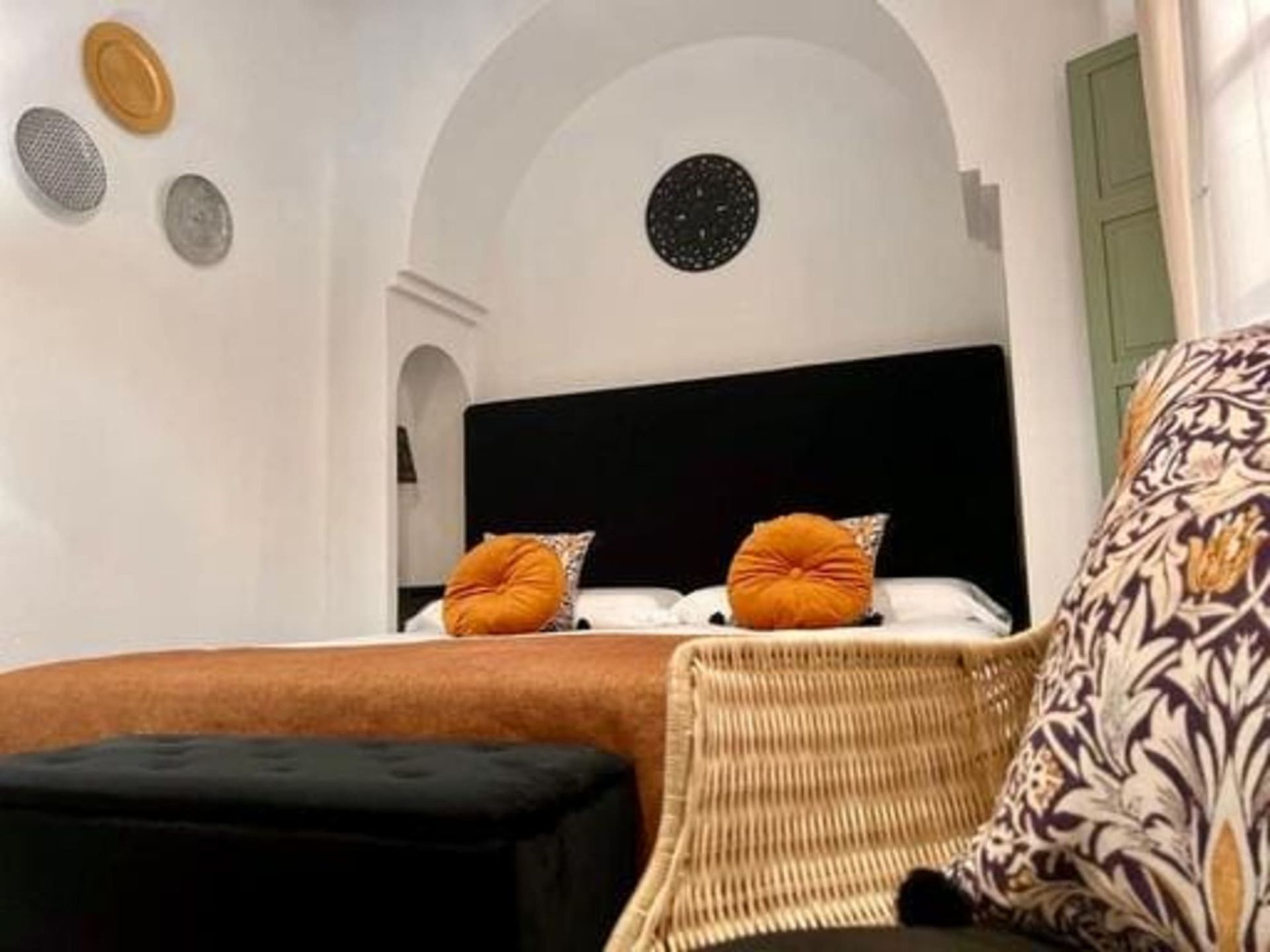 Dormitorio con cama, almohadas naranjas y platos decorativos en la pared.