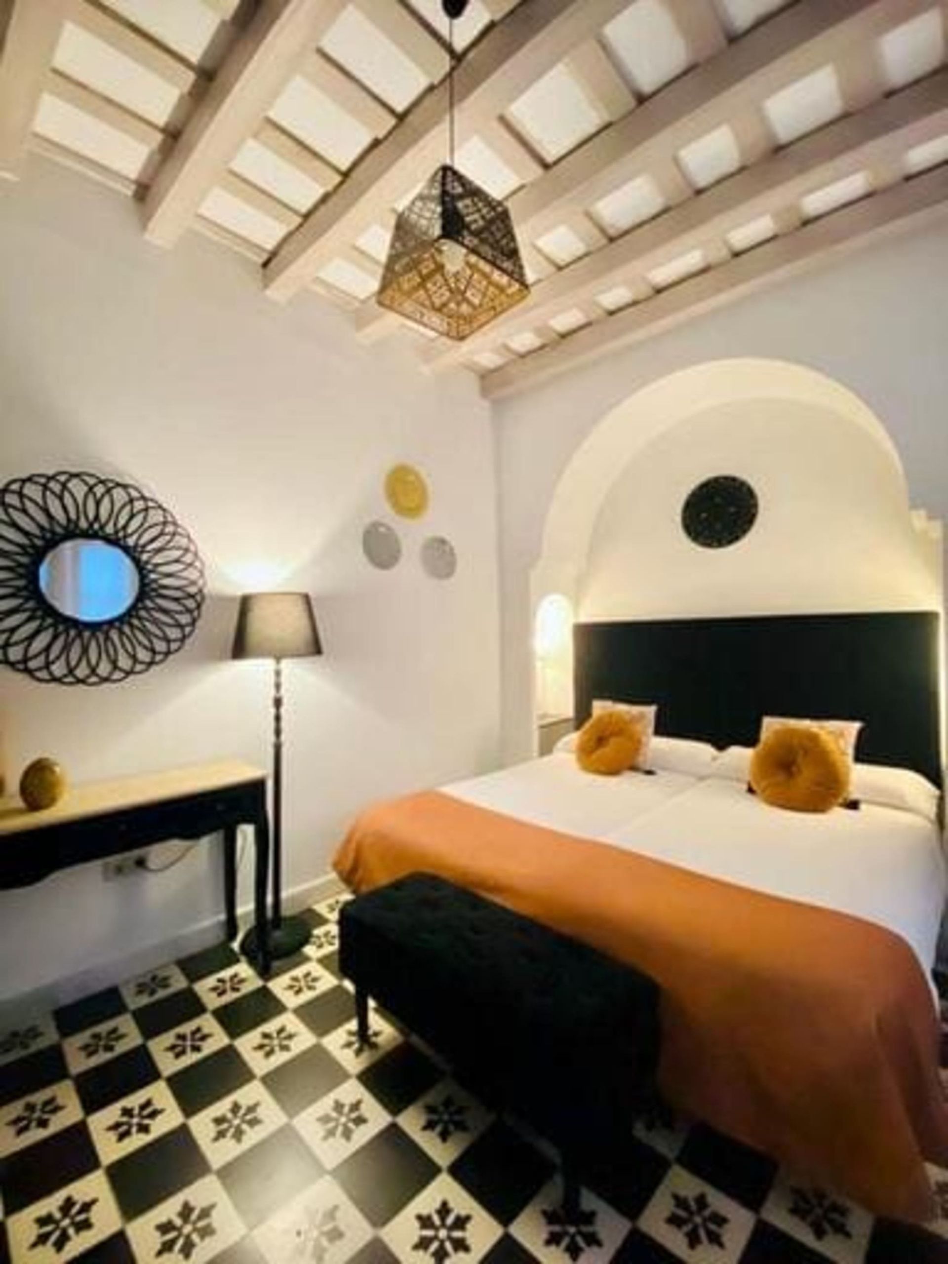 Dormitorio con cama, banco, suelo de baldosas en blanco y negro y elementos decorativos.