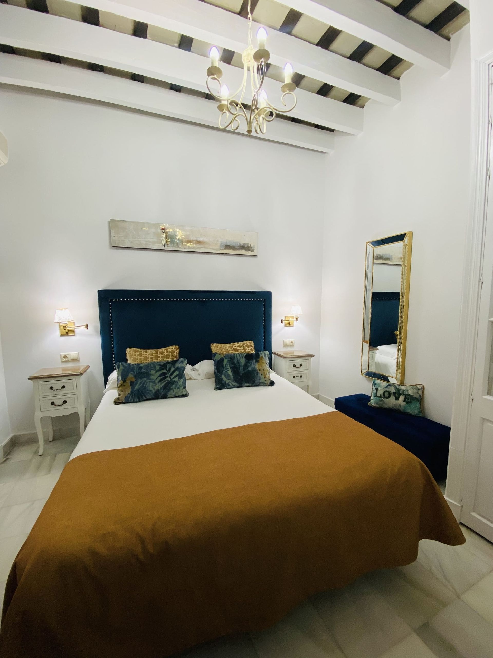 Dormitorio con cabecera azul, detalles dorados, paredes blancas y techo decorativo.