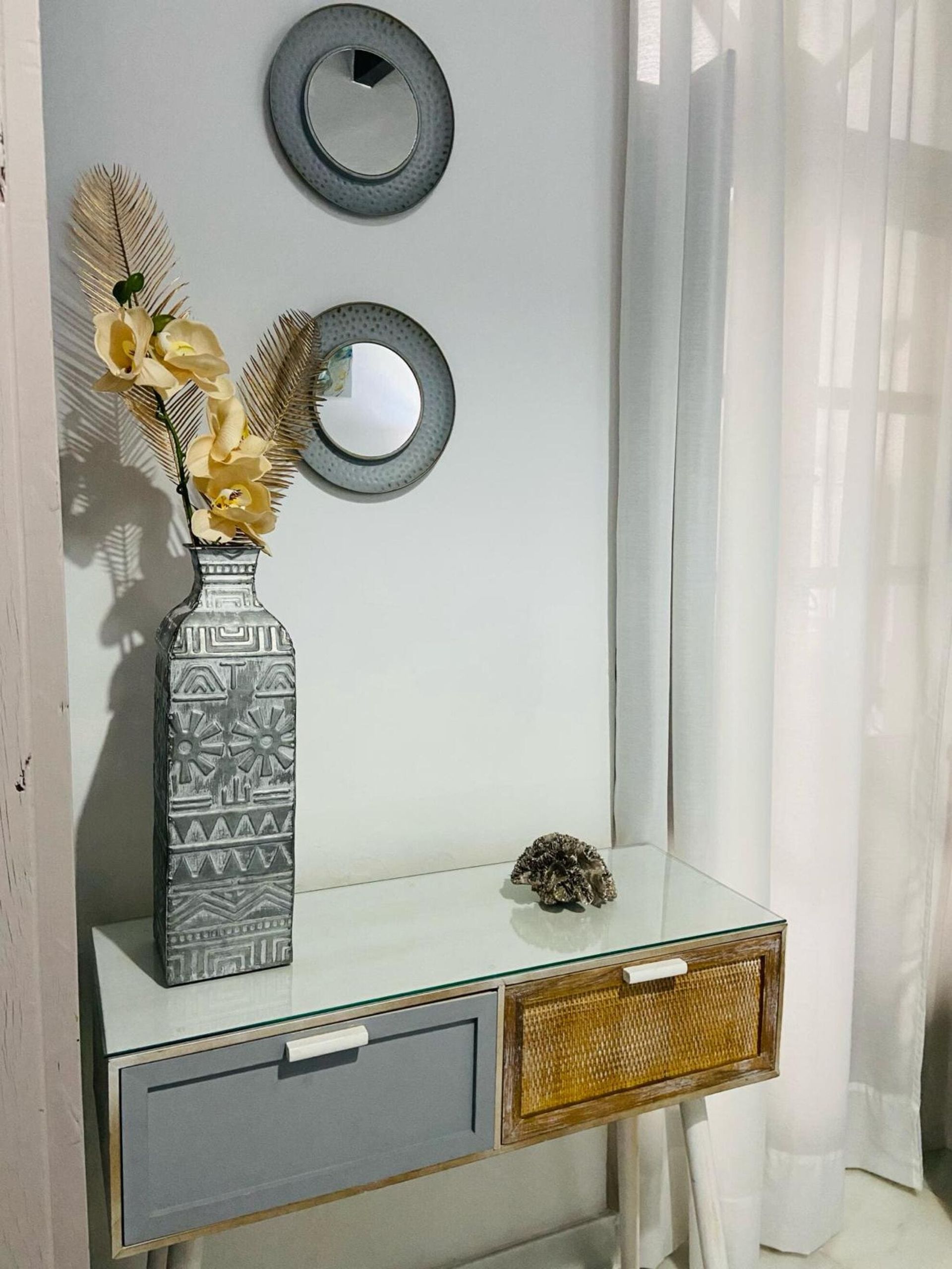 Entrada de paredes blancas con consola flotante, jarrón de flores y dos espejos redondos. 