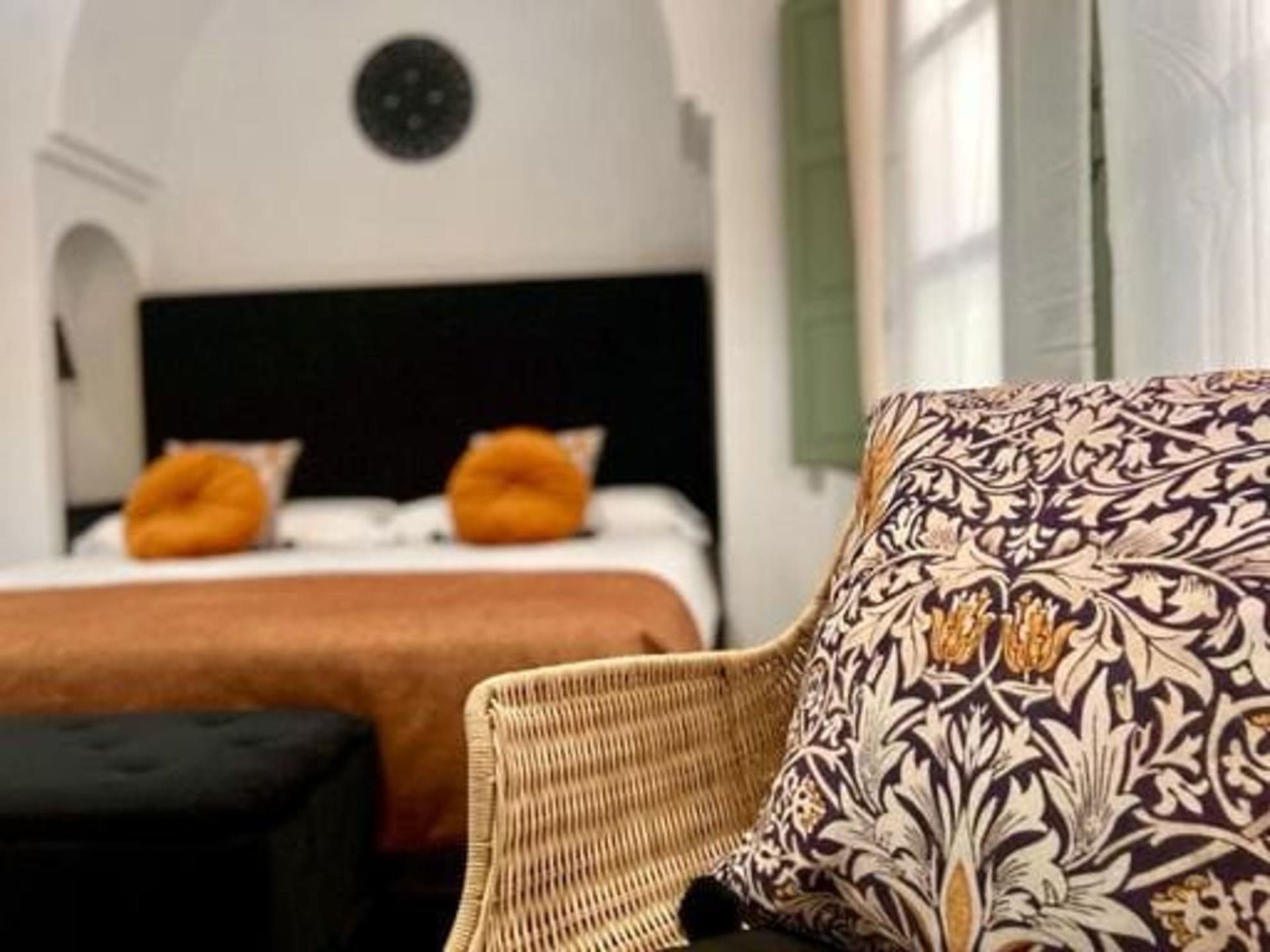 Interior de dormitorio con cama, silla de mimbre, almohada estampada y detalles en naranja.