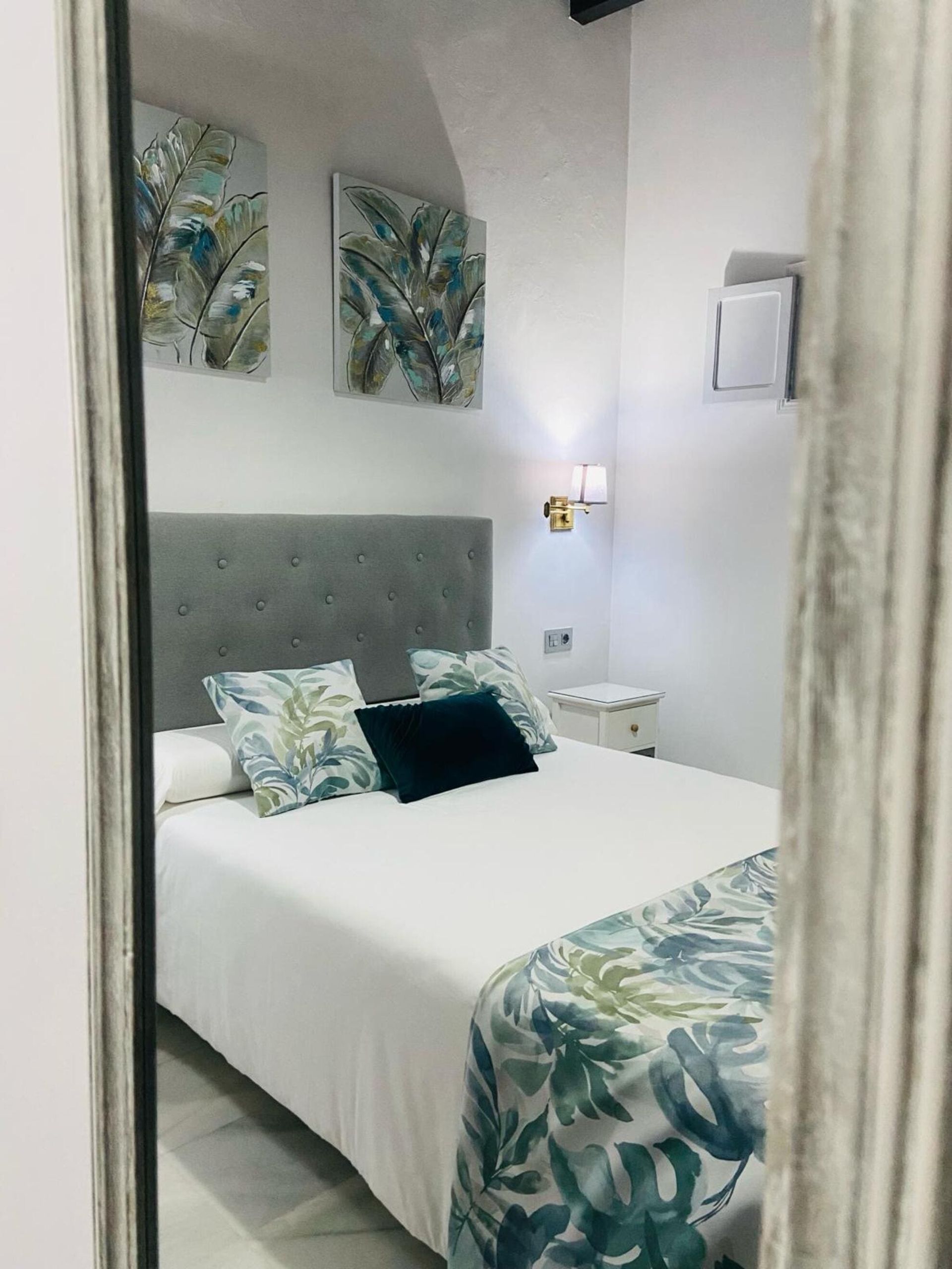 Dormitorio con paredes blancas, cama con cabecero gris y arte decorativo.