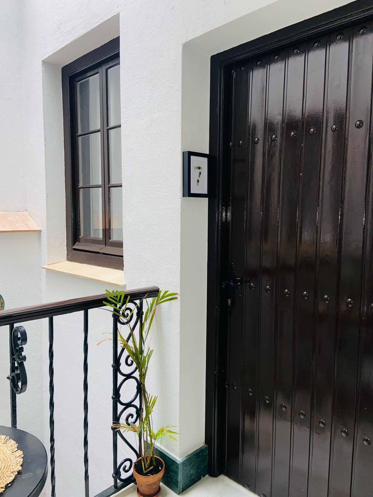 Exterior: Puerta, ventana y balcón de color marrón con planta en maceta sobre una pared de estuco blanco.