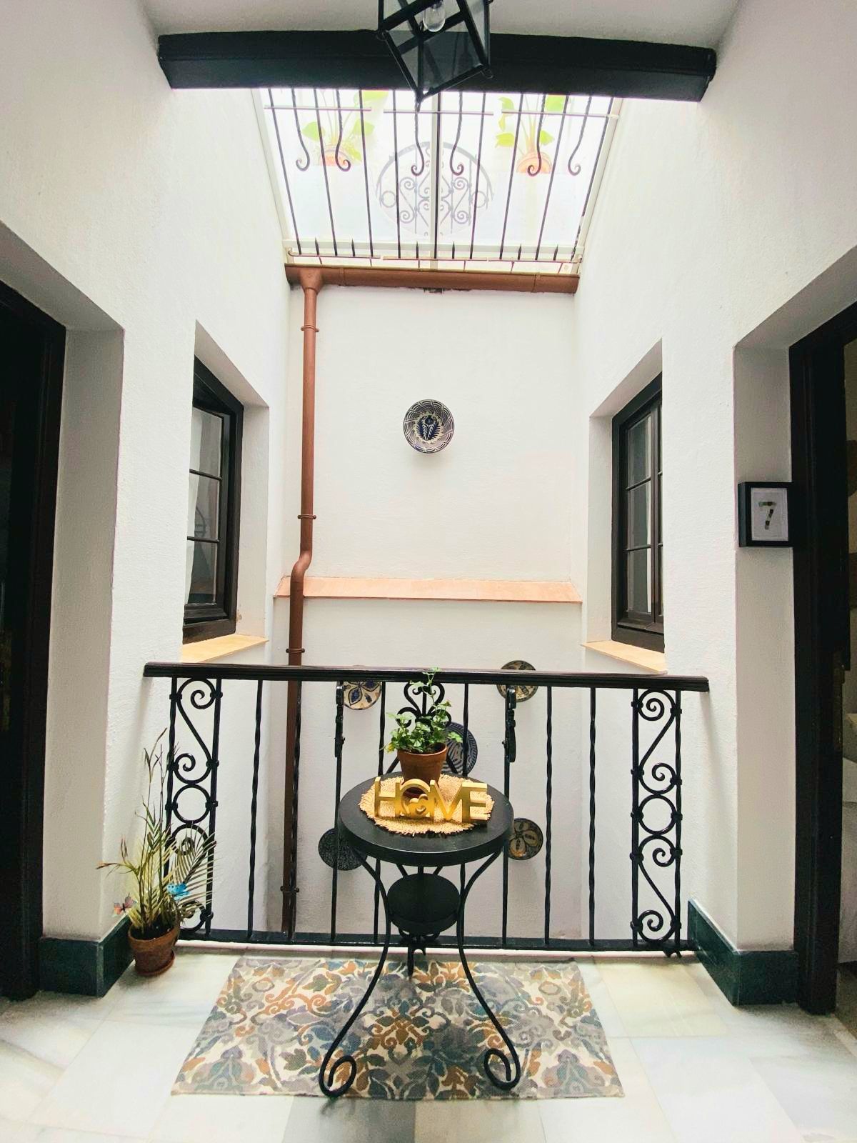 Patio interior con techo de cristal y detalles en hierro forjado, mesa y alfombra.