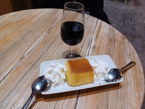 Pastel con crema batida y una copa de vino tinto sobre una mesa de madera.