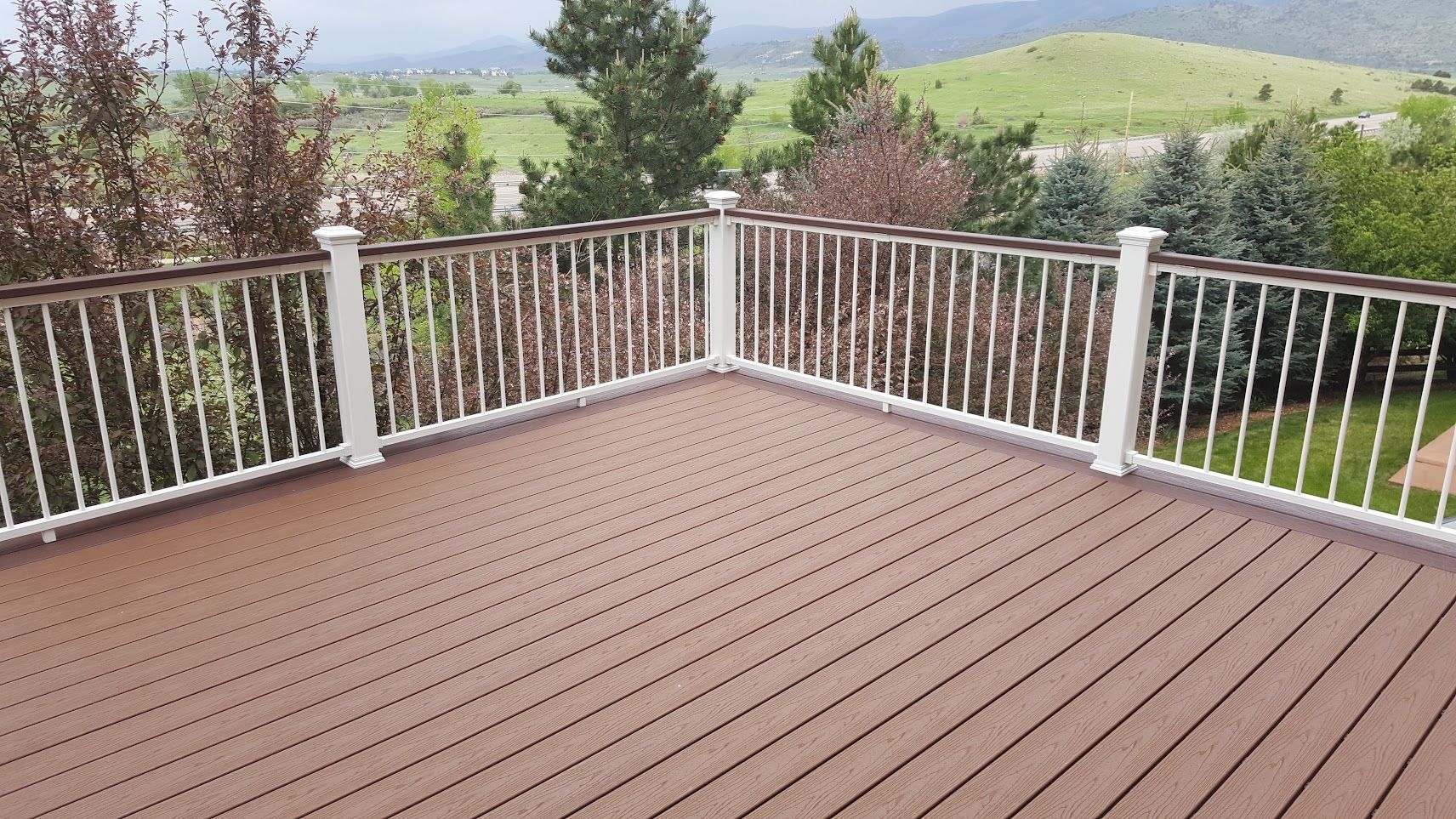 A wooden deck with a white railing and a view of the mountains.