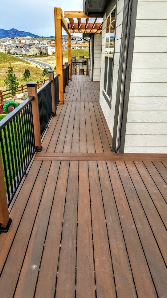 A wooden deck with a black railing is leading to a house.