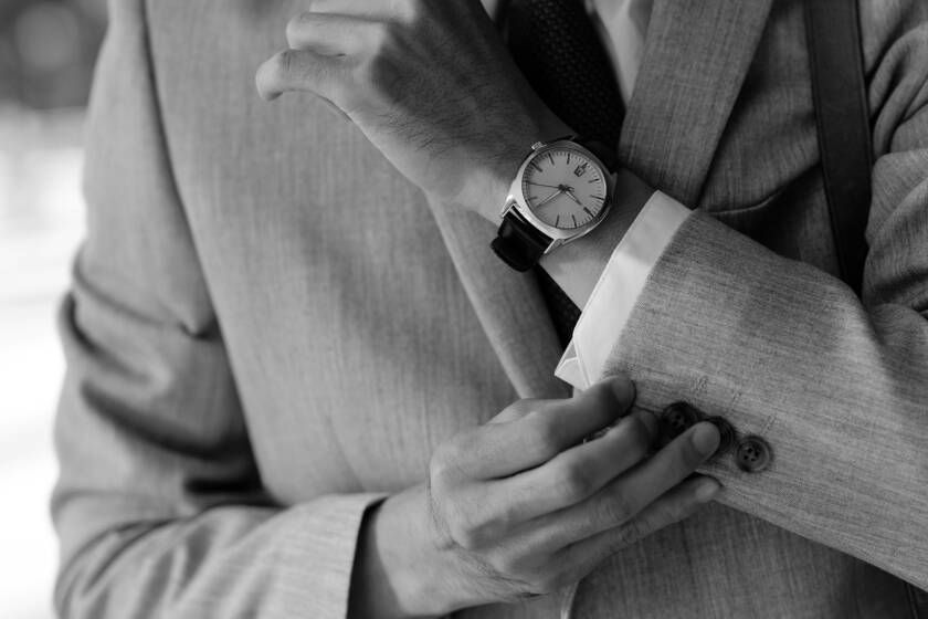 Man in a suit adjusting his sleeve, watch visible on his wrist. Black and white.