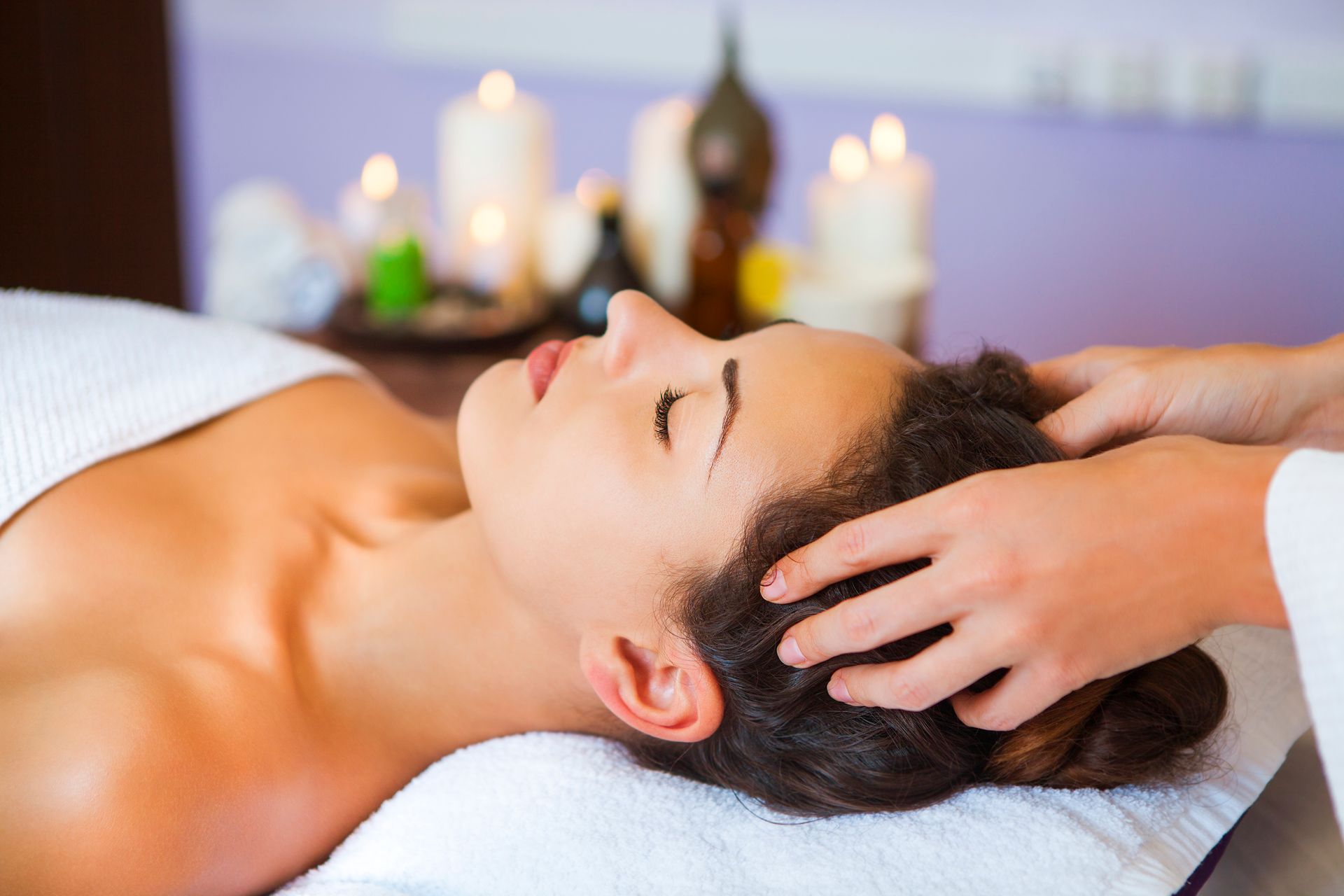 Woman receiving a head massage in a spa setting with candles.