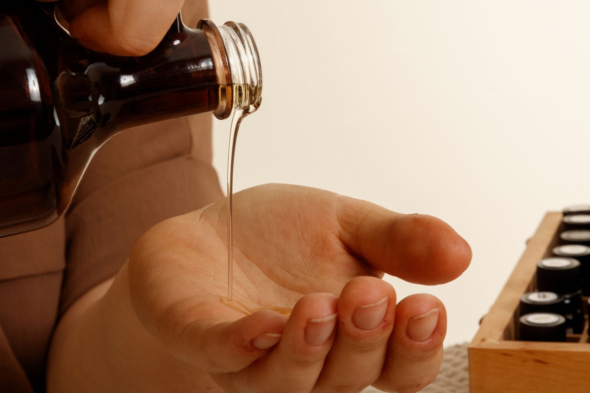 Hand pouring oil from a brown bottle into an open palm, with other bottles in the background.