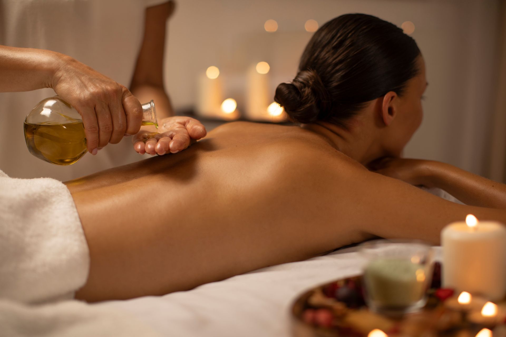 Woman receiving back massage with oil in spa-like setting with candles.