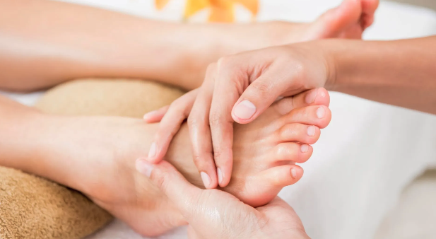 Hands massaging a foot on a spa table, with a flower in the background.