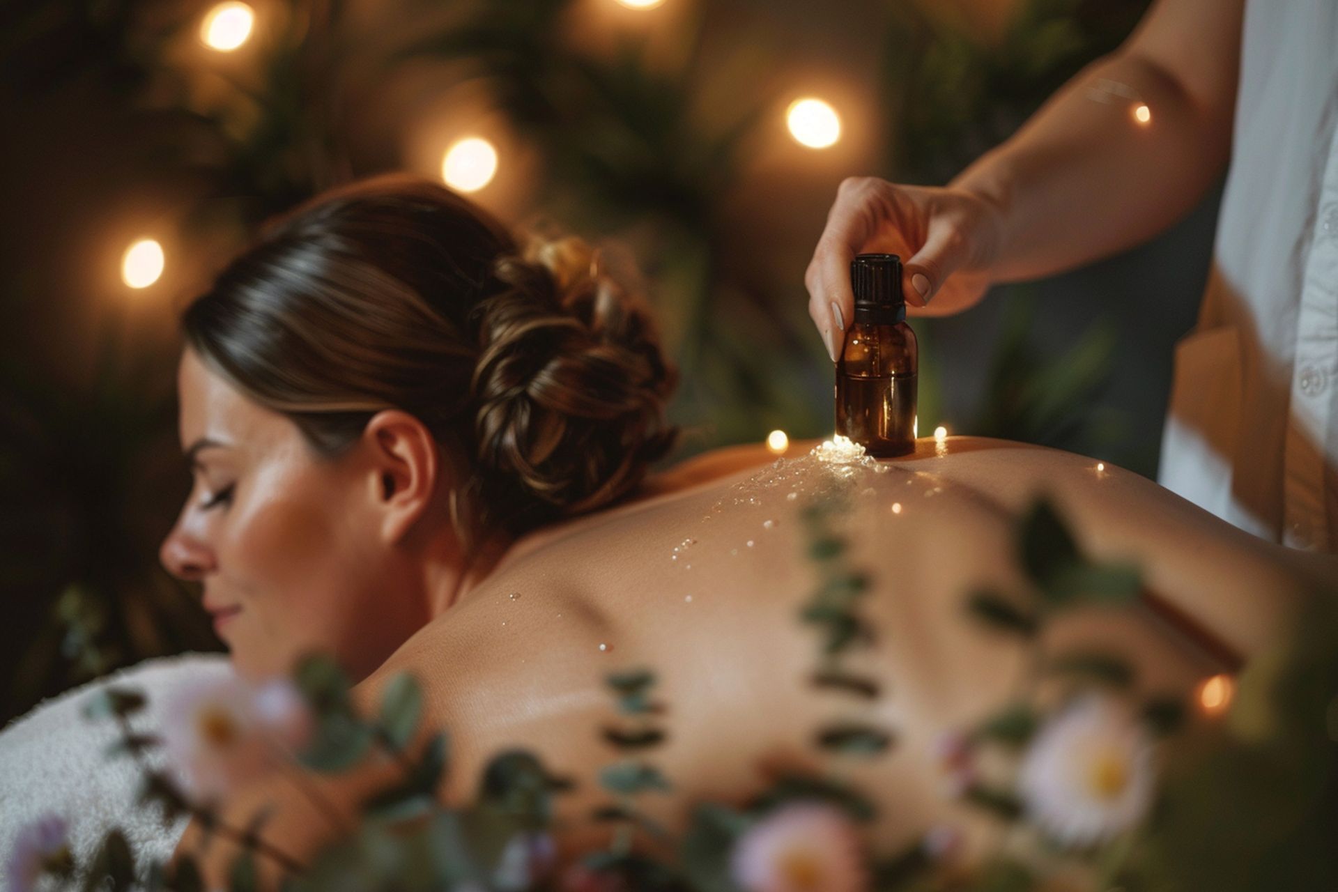 Woman receiving massage with oil, surrounded by lights and flowers.