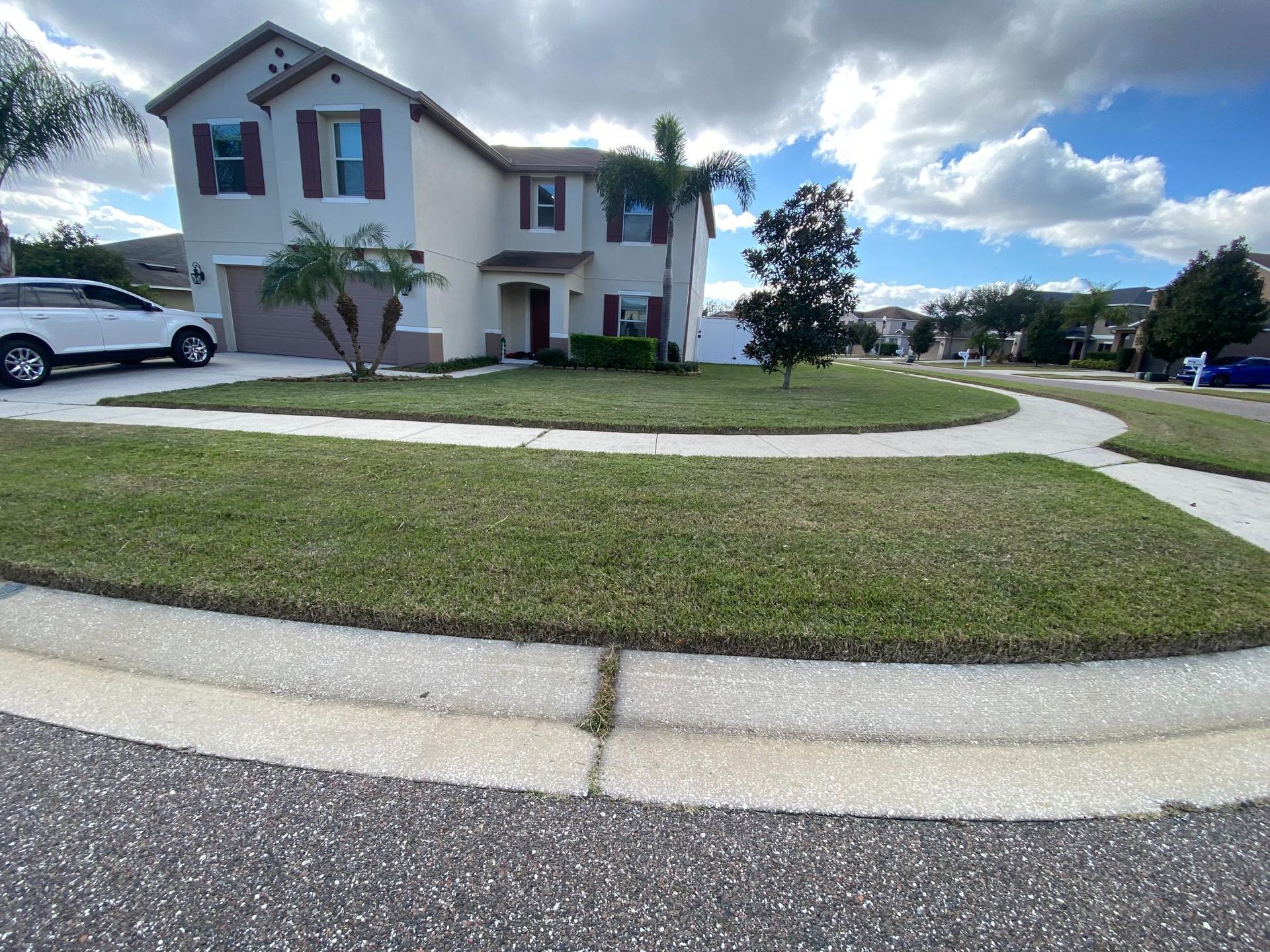 Two-story house with green lawn and curb. Cloudy sky above. White SUV parked in driveway.