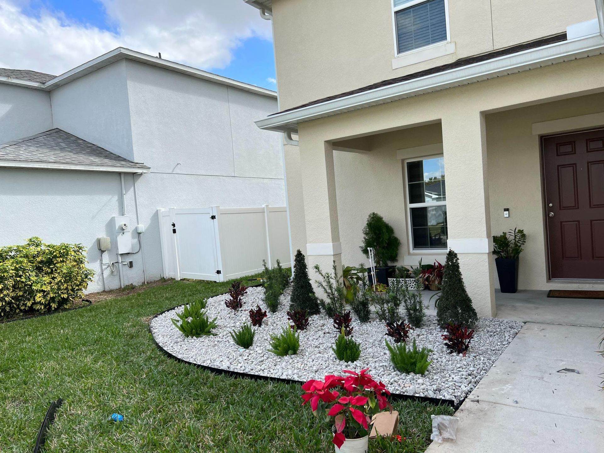 Front yard with a flower bed, white stone, plants, and a beige house.