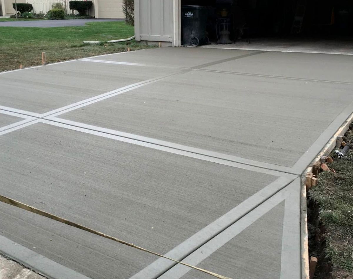 Freshly poured concrete driveway with expansion joints, next to a garage.