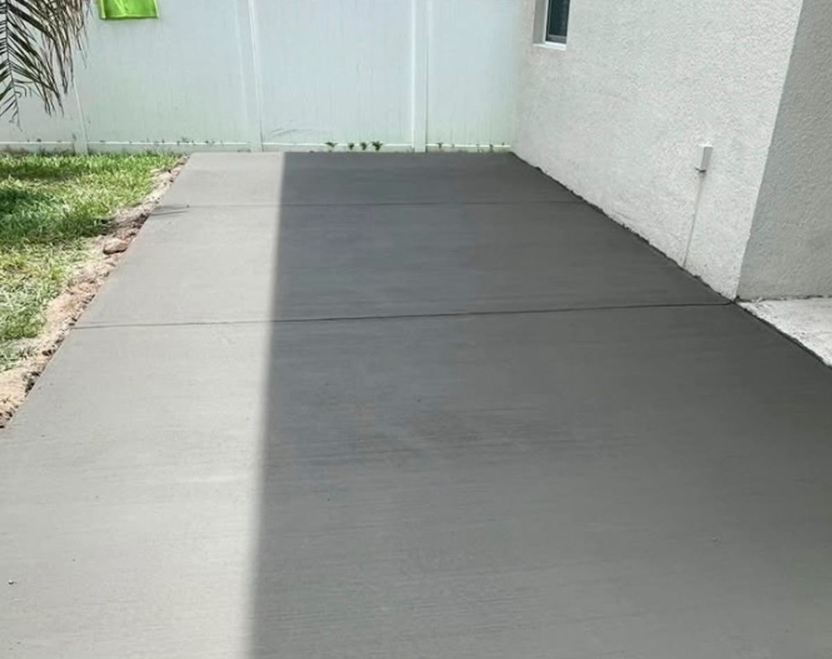 Newly poured concrete patio next to a white wall, leading to a grassy area.