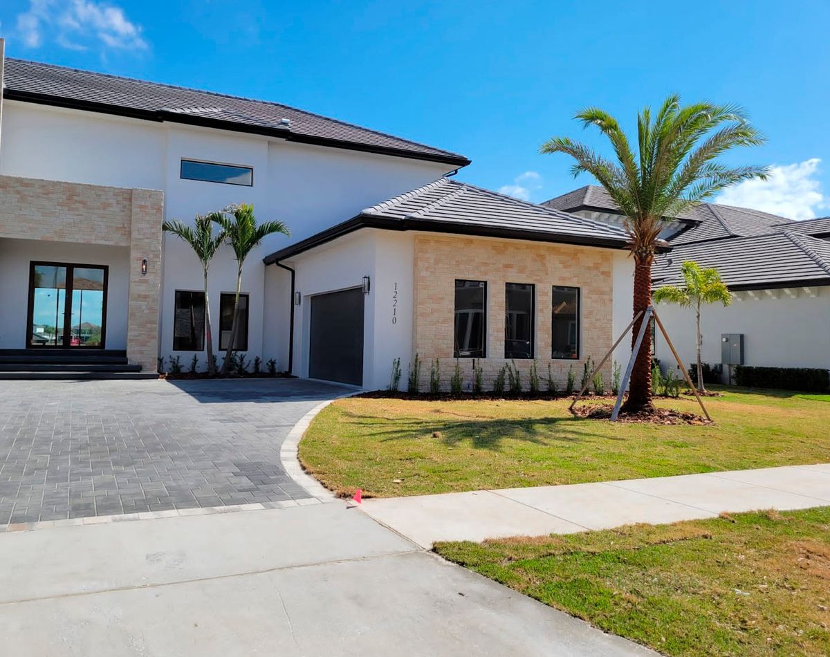 Modern white house with a driveway, garage, and landscaping under a blue sky.