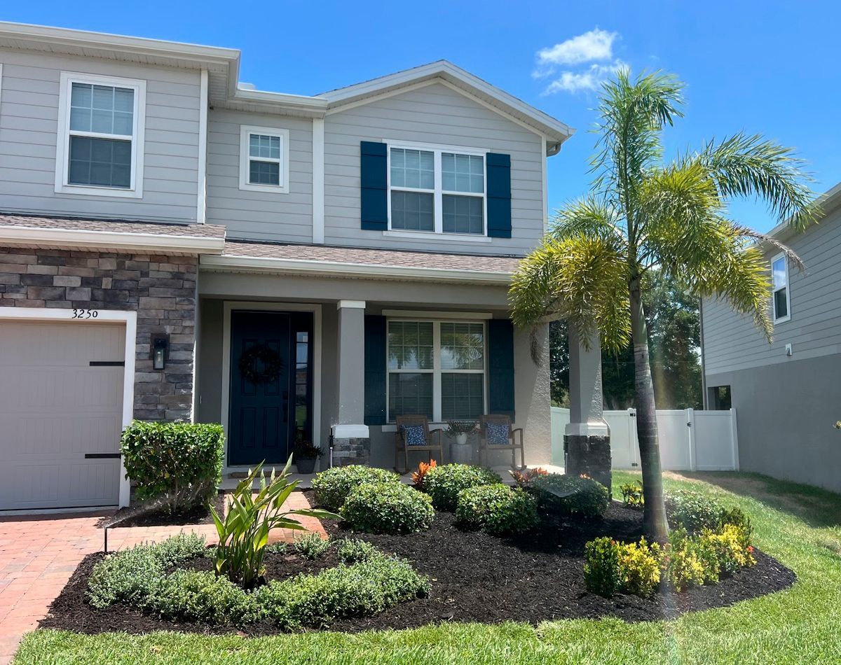 Two-story home with a gray exterior, dark blue shutters and door, and landscaping in front of a blue sky.