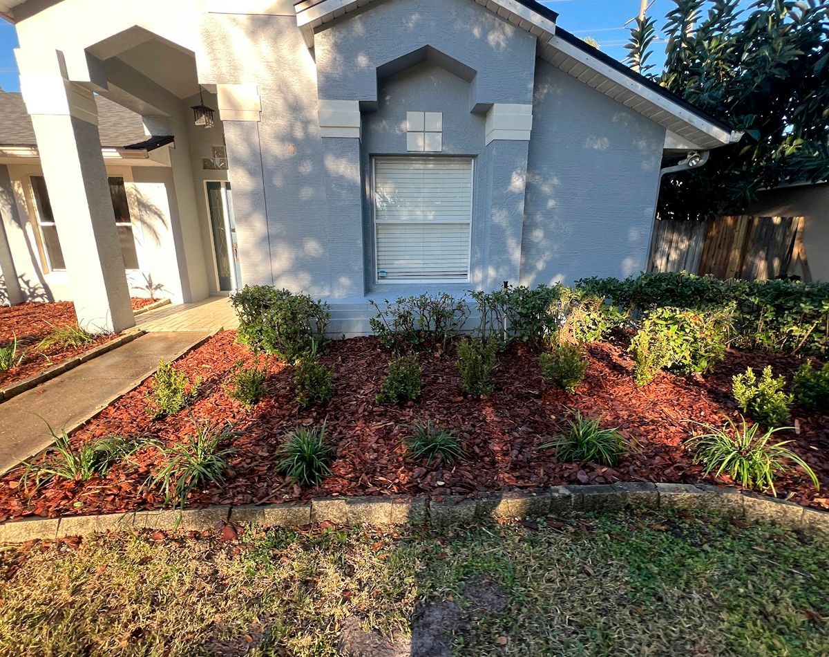House exterior with garden beds and mulch, with a driveway in front and lawn.