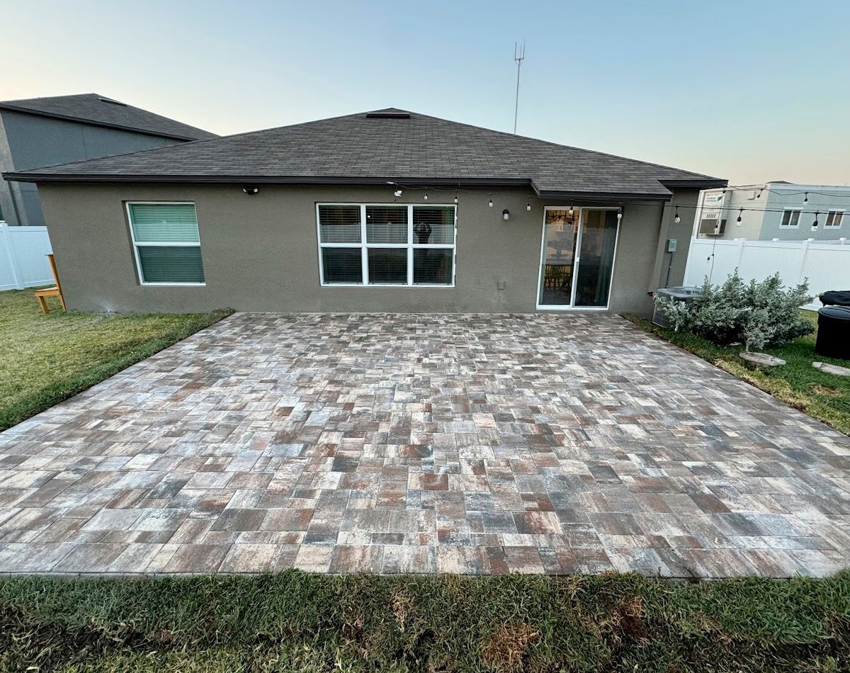 Backyard with a brick patio, house, and green grass.