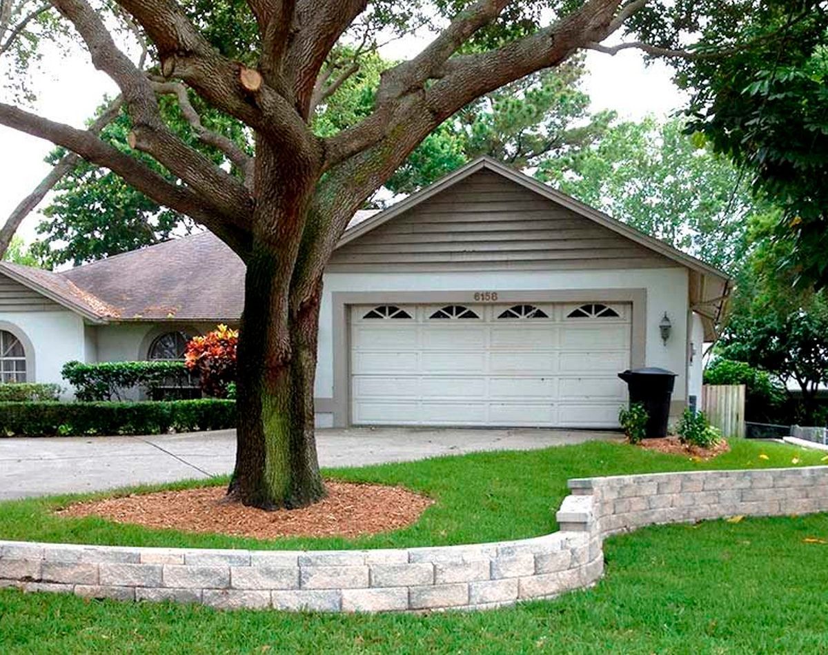 House with a garage, large tree in the yard, and a short retaining wall.