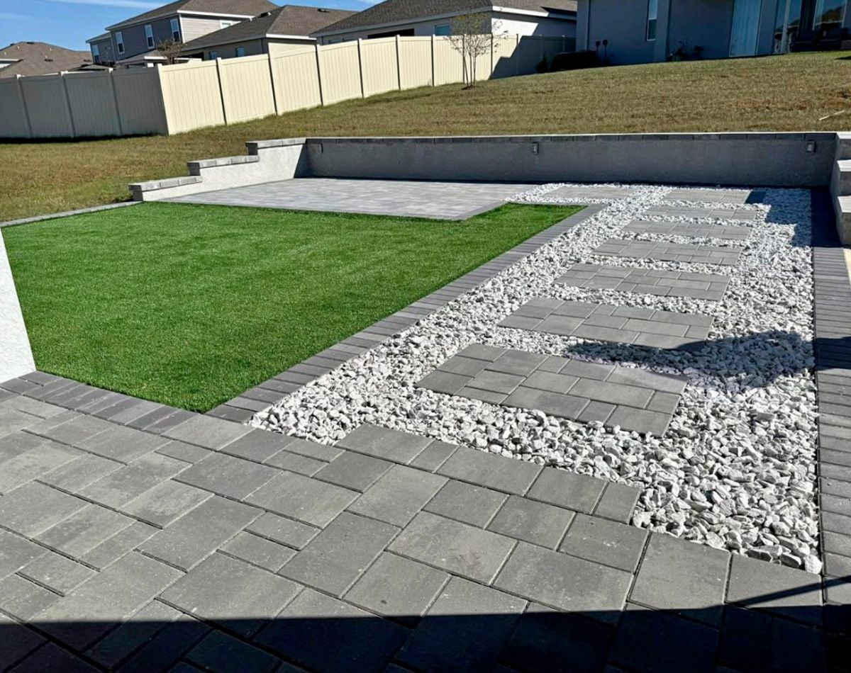 Backyard patio with gray pavers, white gravel, and artificial green grass.