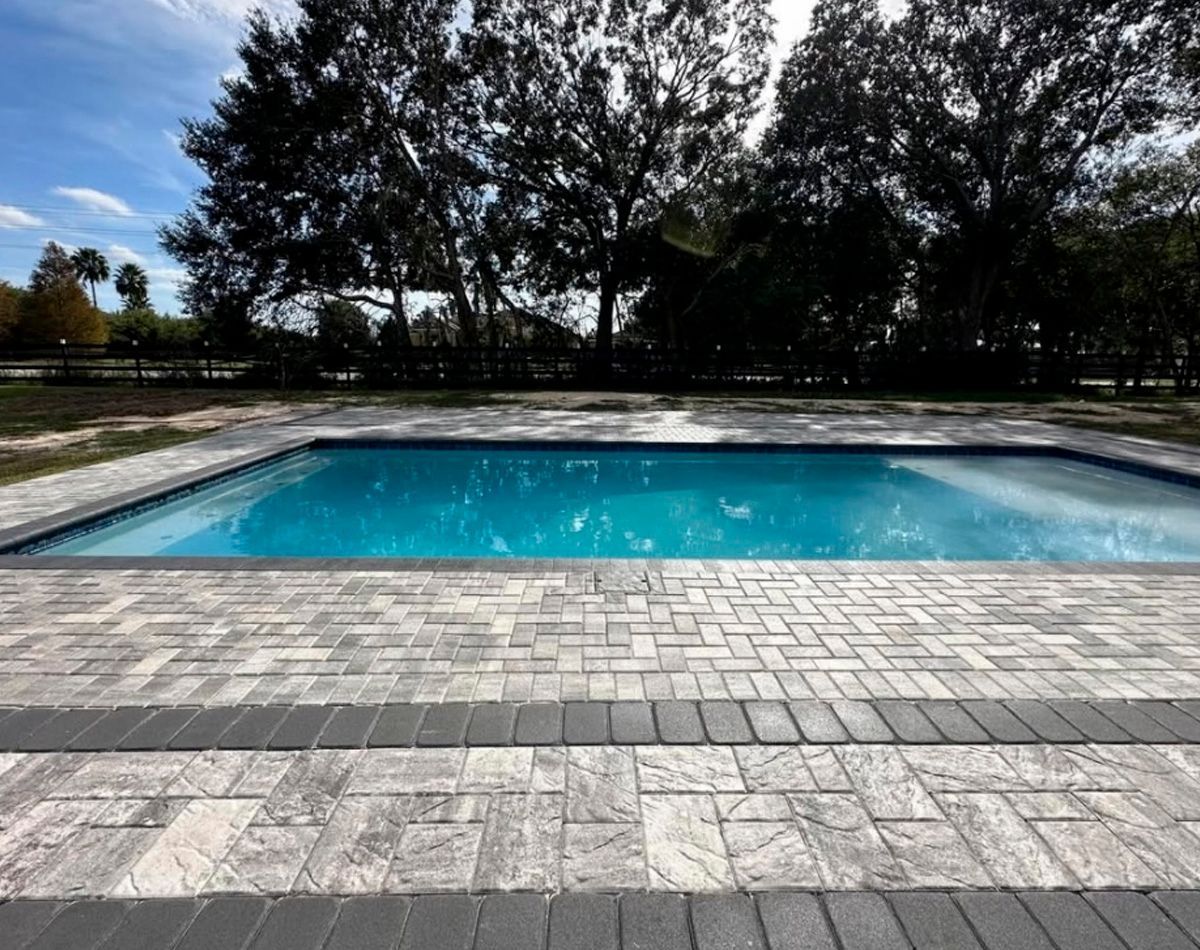 Swimming pool with brick pavers; trees in the background under a blue sky.