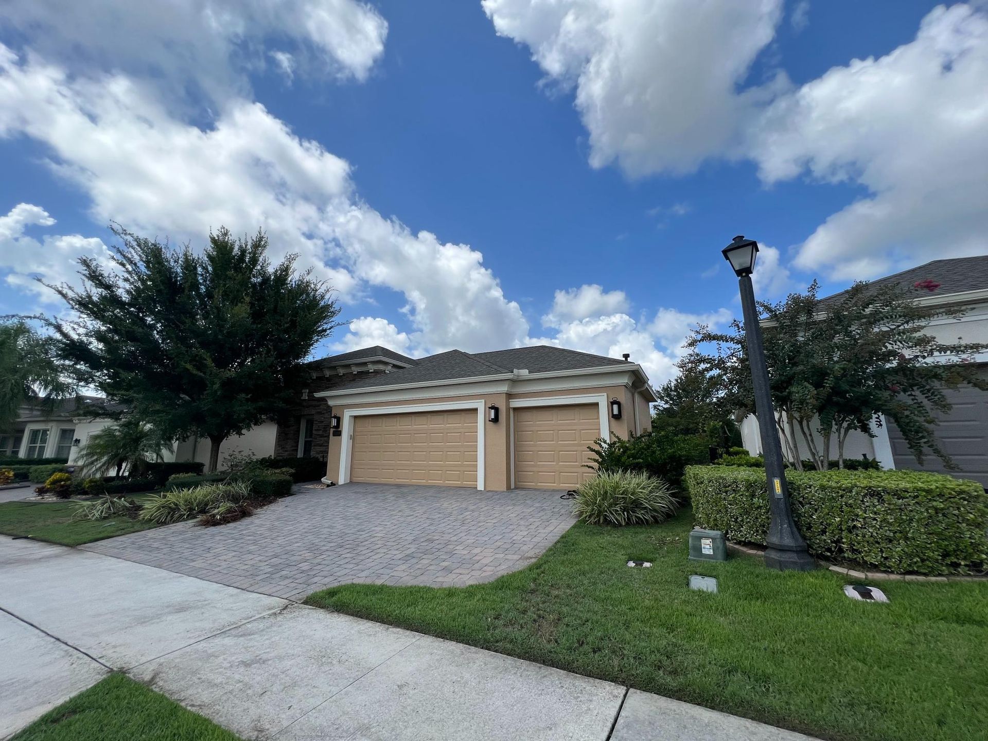House with two-car garage, gravel driveway, green lawn, trees, and blue sky with clouds.