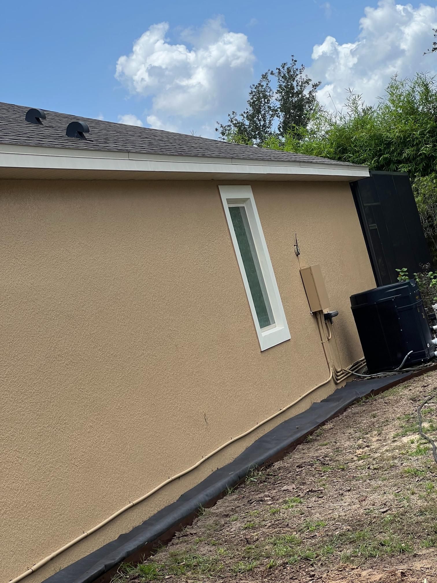 Tan stucco building with a window and black air conditioner against a blue sky.