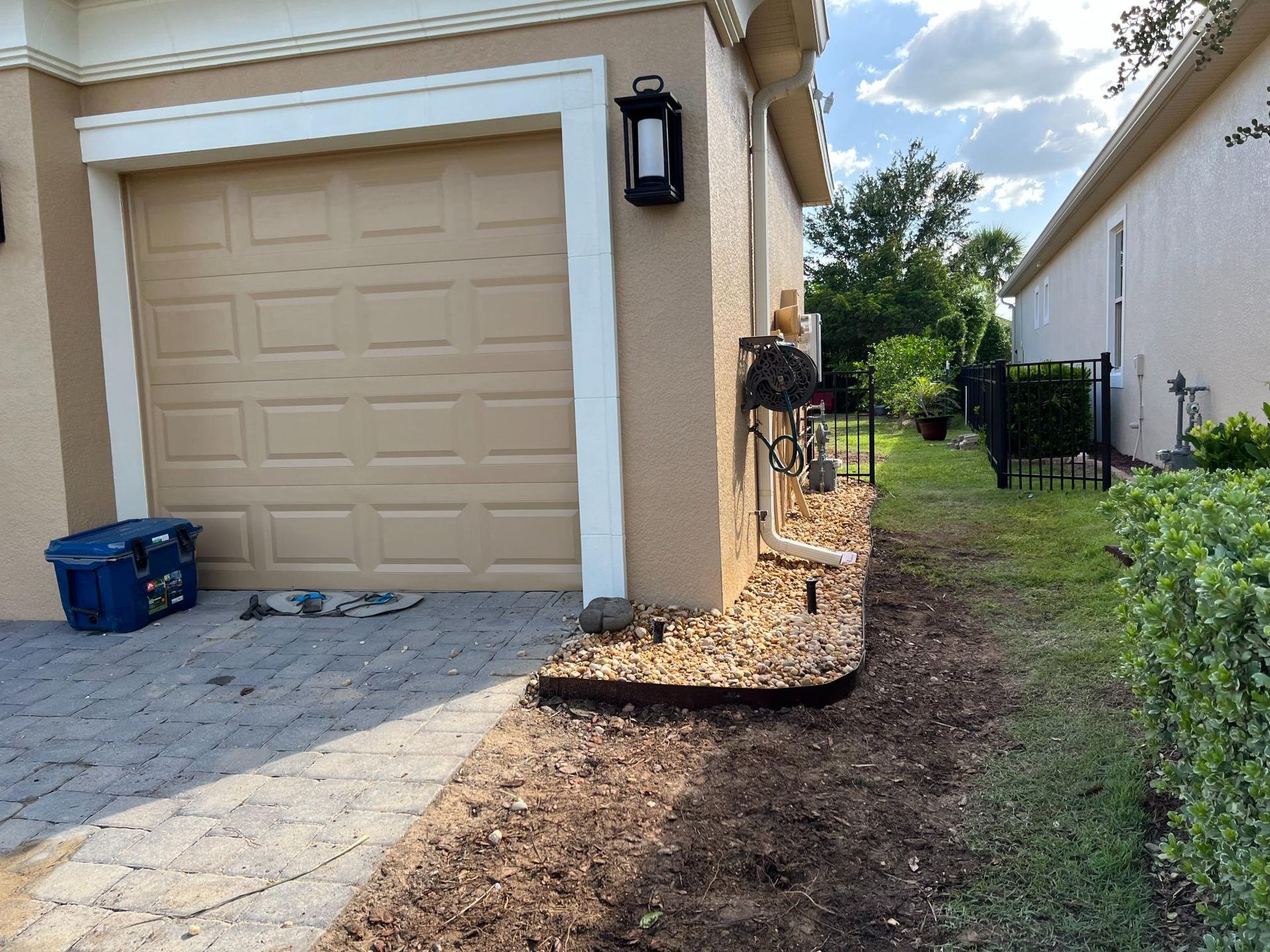 Garage exterior with tan door, stone driveway, and garden bed filled with rocks and mulch.