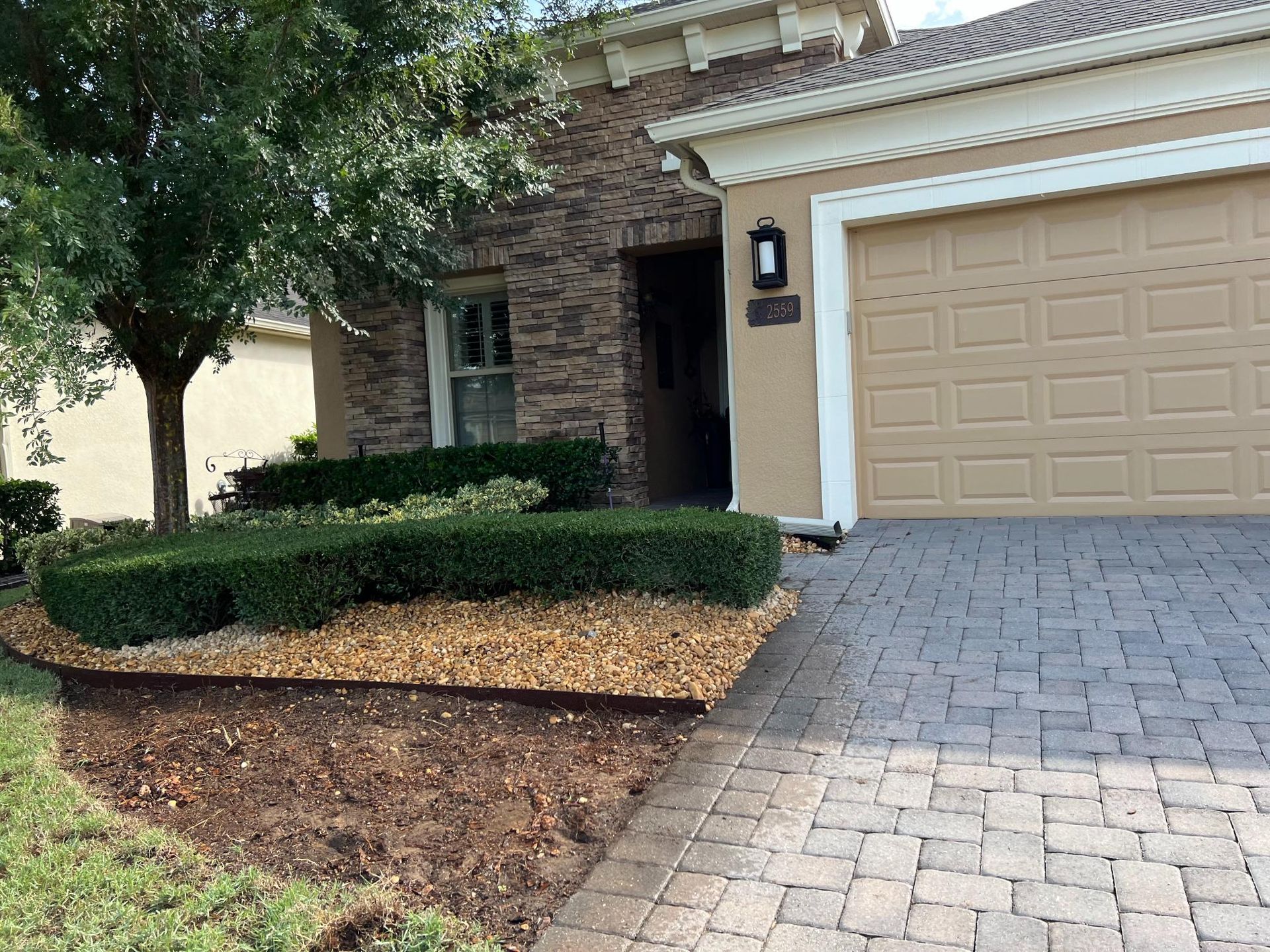 House exterior with stone facade, tan garage door, and manicured landscaping.