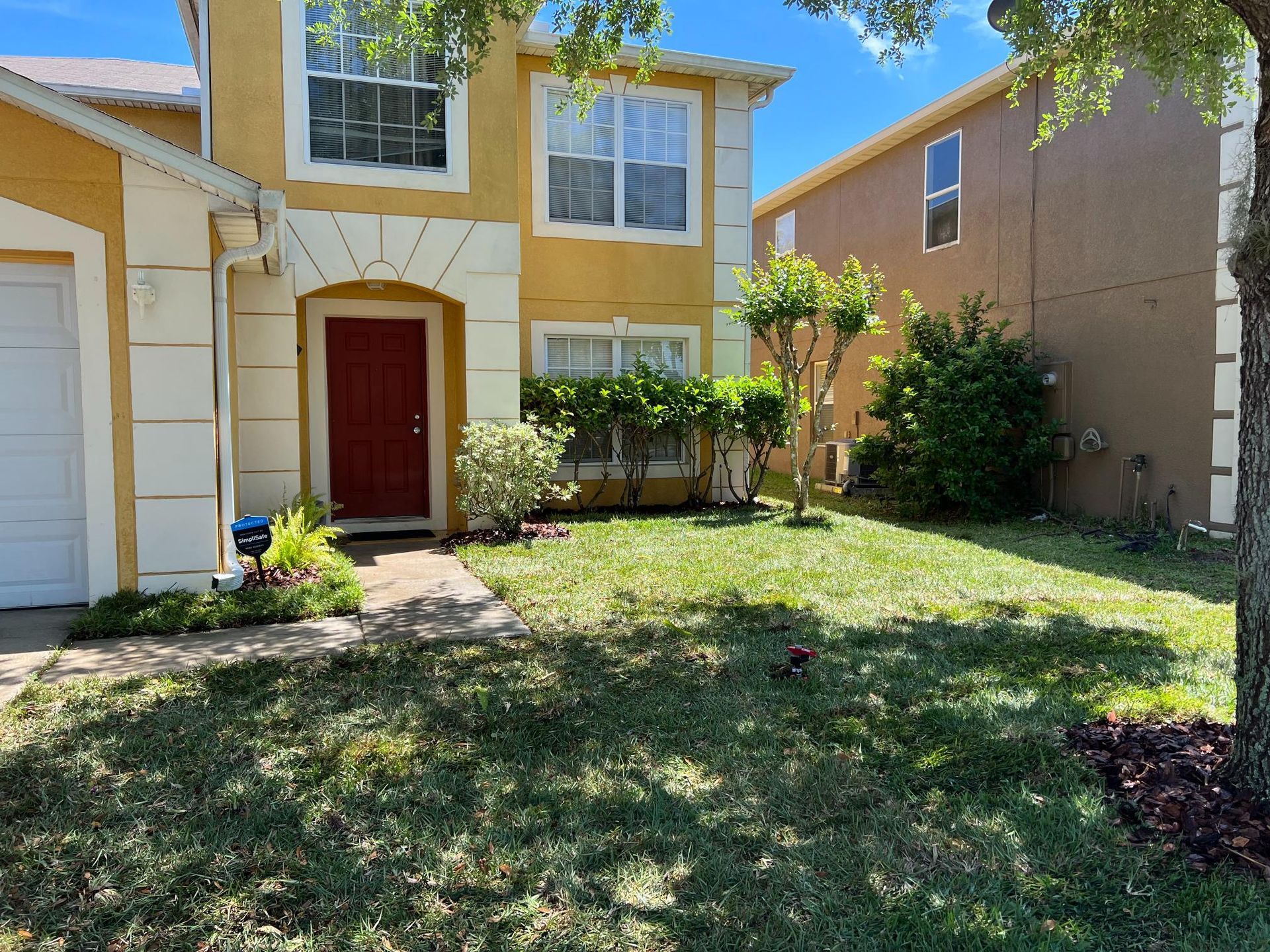Yellow two-story house with red door, white trim, and a small front yard with green grass.