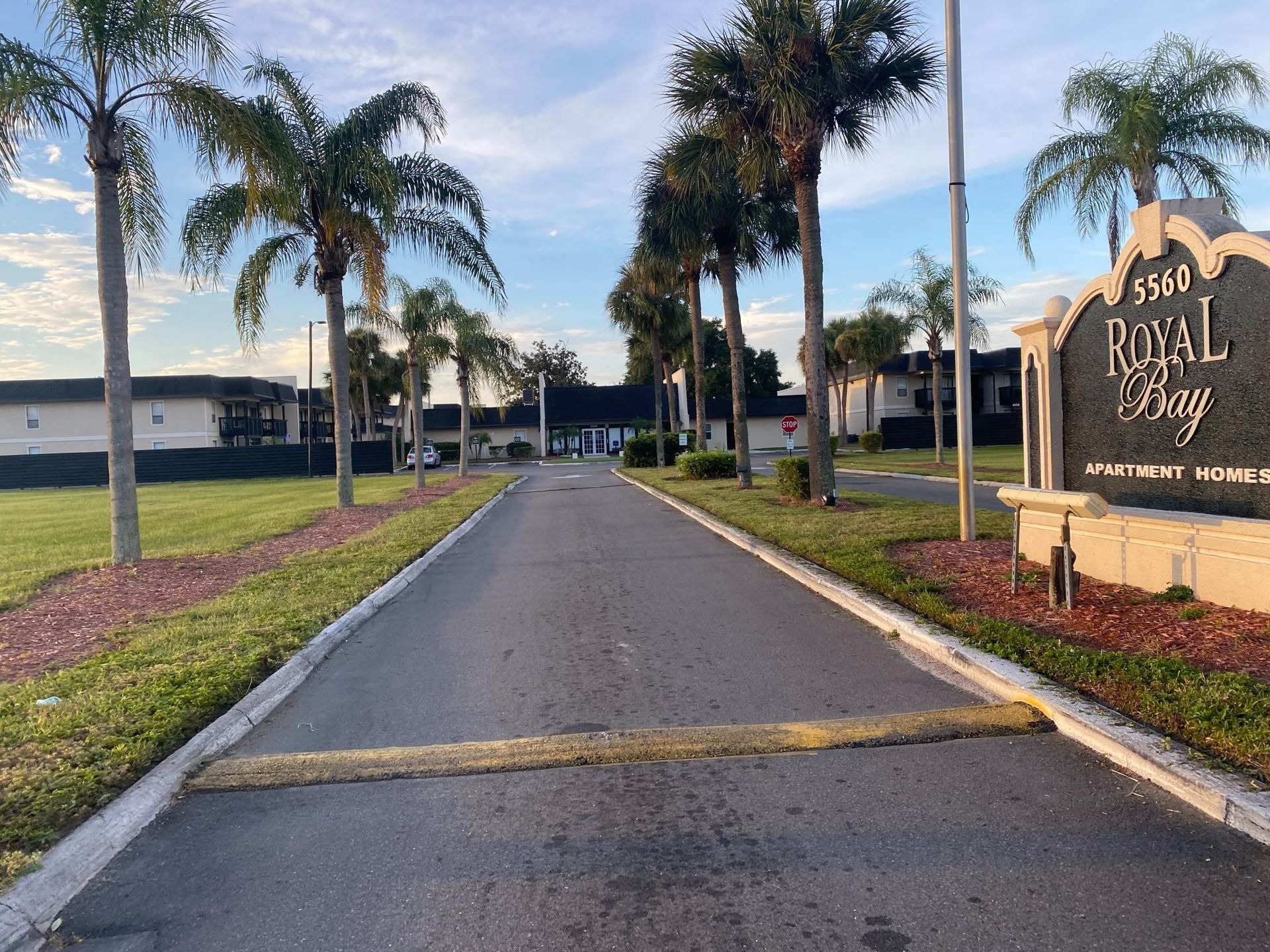 Entrance to Royal Bay Homes, asphalt road, palm trees, green grass, sign on the right.