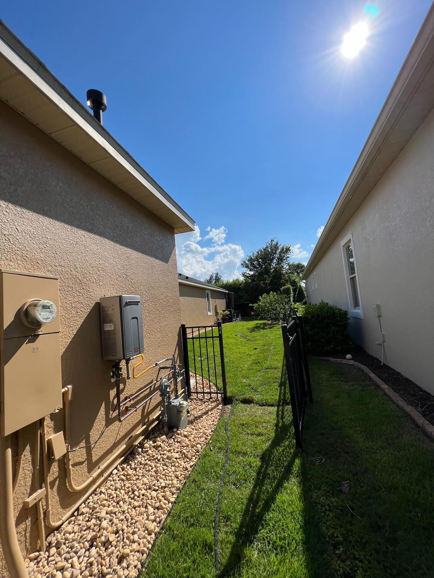 A narrow walkway between two beige houses with a black gate at the end, sunny day.