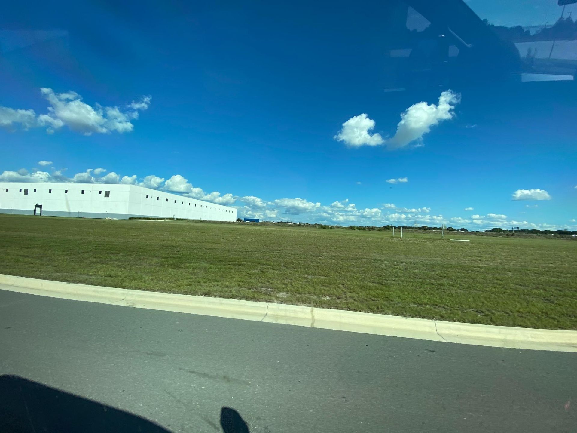 A large white building on a grassy field under a bright blue sky with scattered clouds.