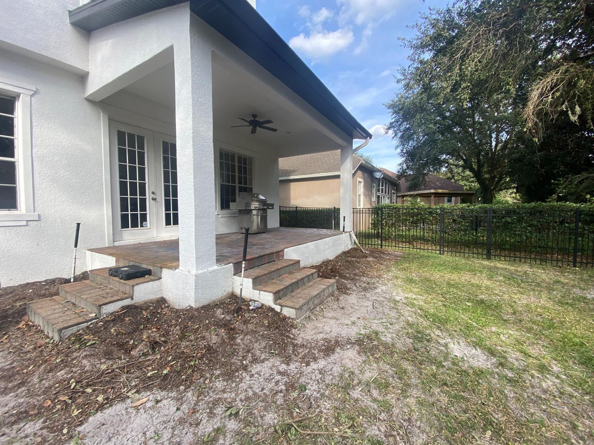 Back patio with steps, grill, and view of yard with fence and trees.