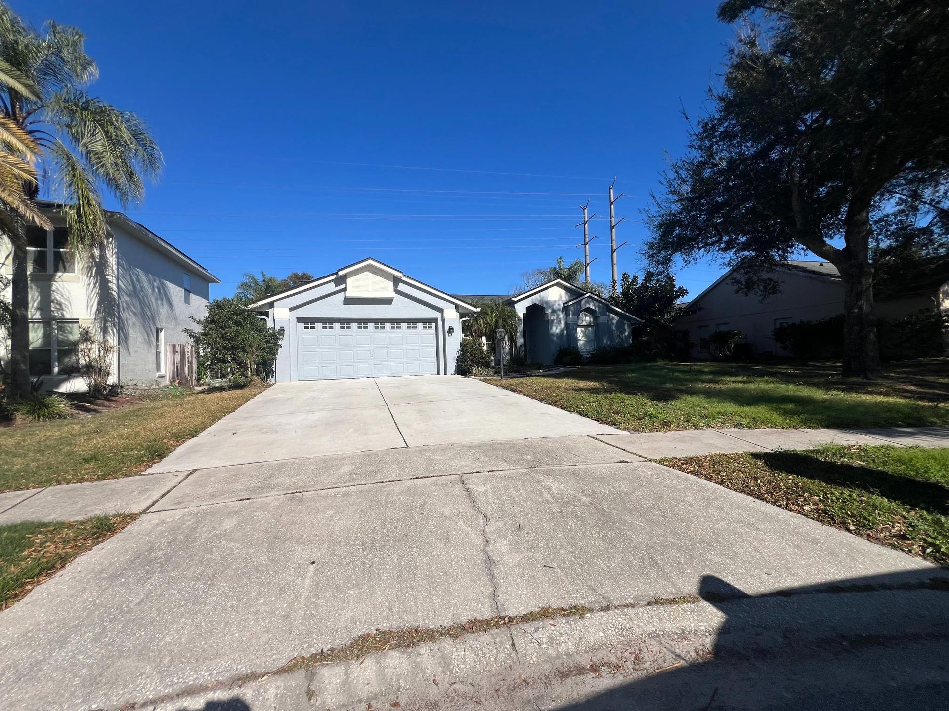 A single-story house with a driveway. Blue sky overhead. Garage and yard are visible.
